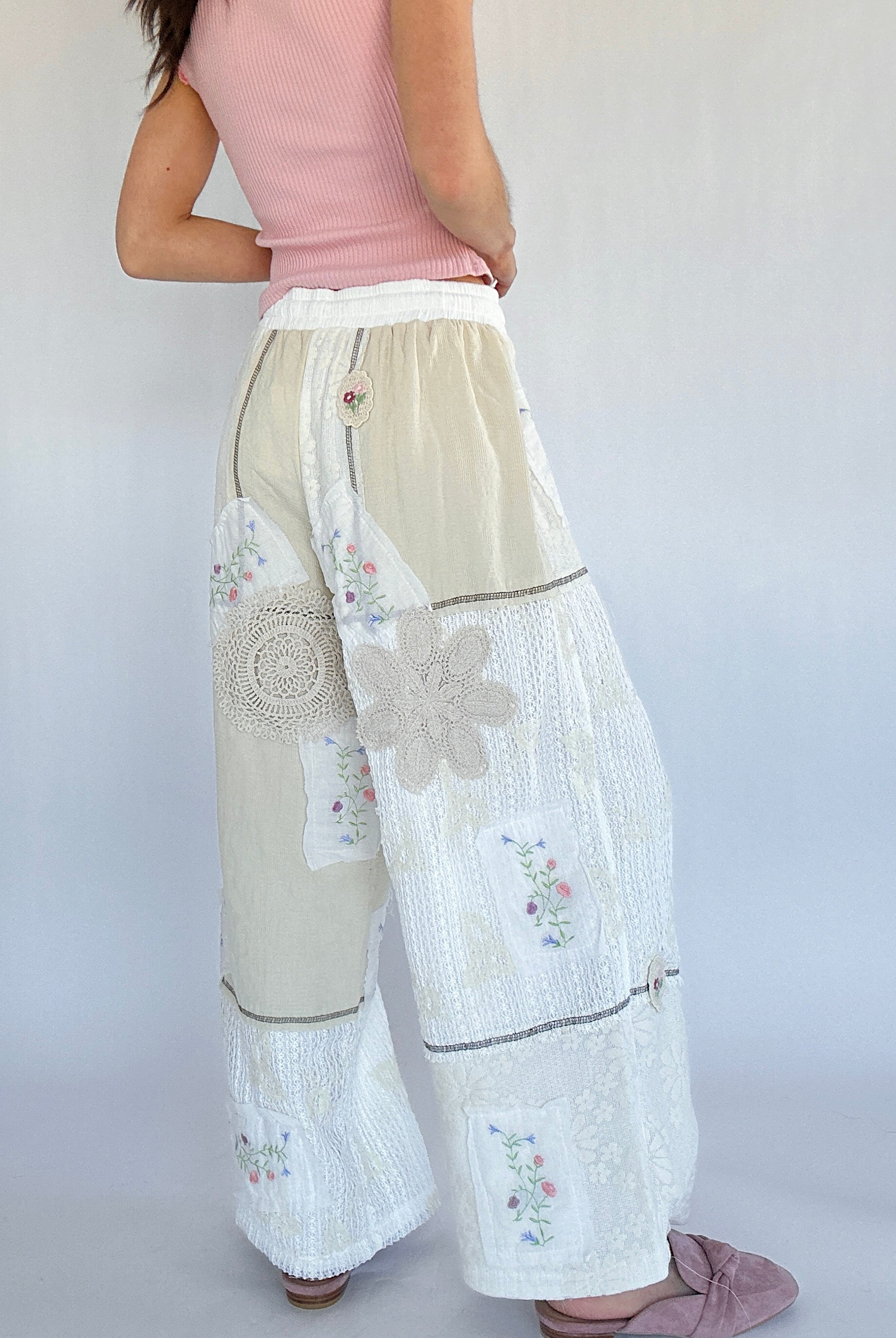 Woman wearing a pink top and beige floral pants on a plain background from back