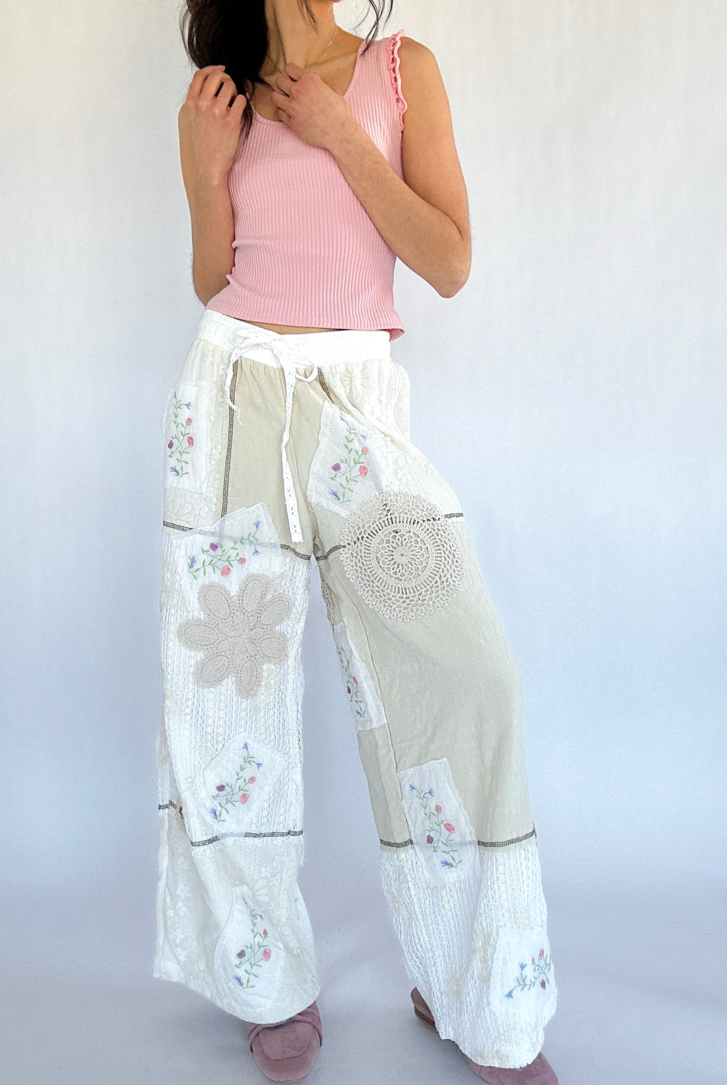 Woman wearing a pink top and white floral pants on a plain background