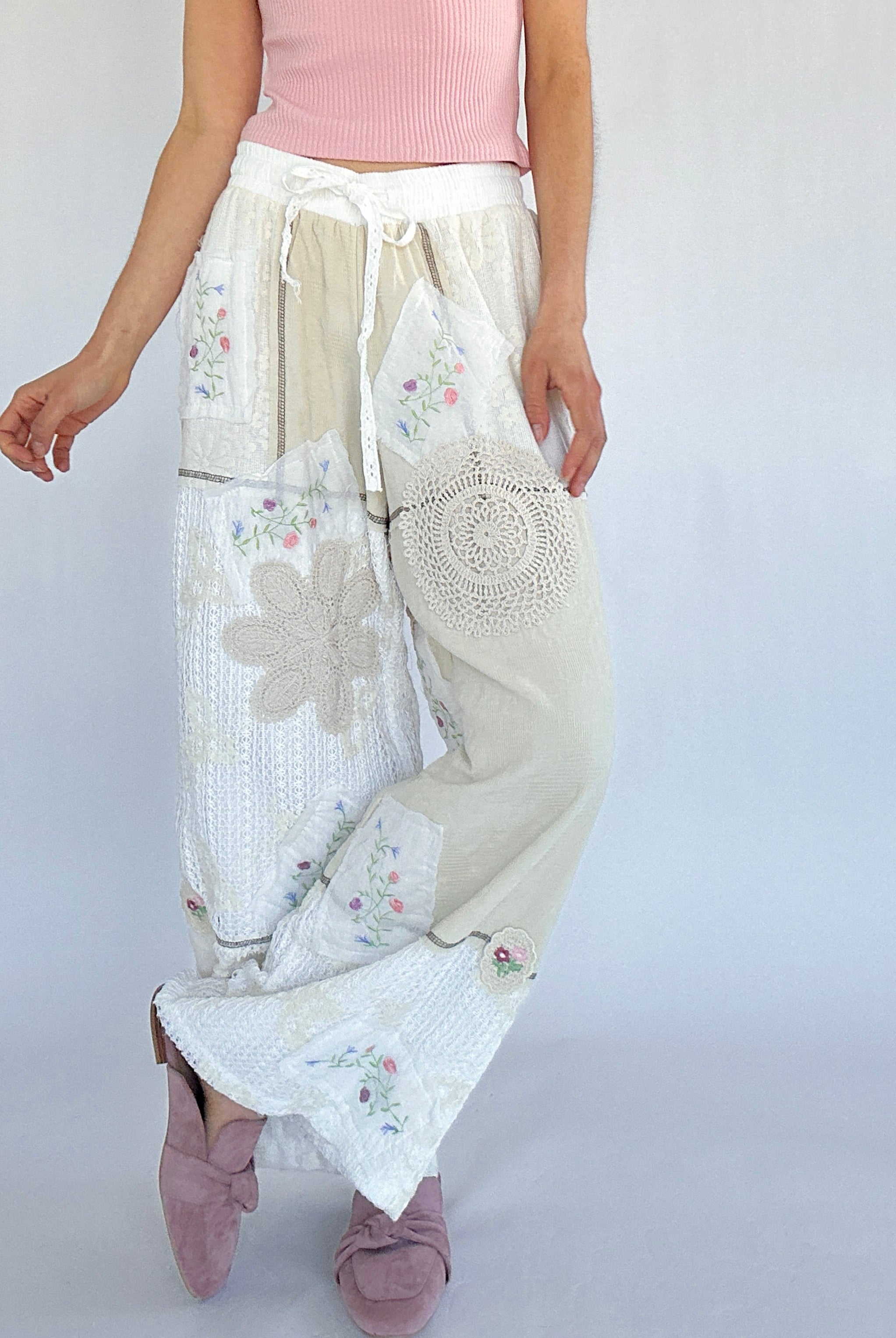 Person wearing a white embroidered pants with floral patterns on a plain background