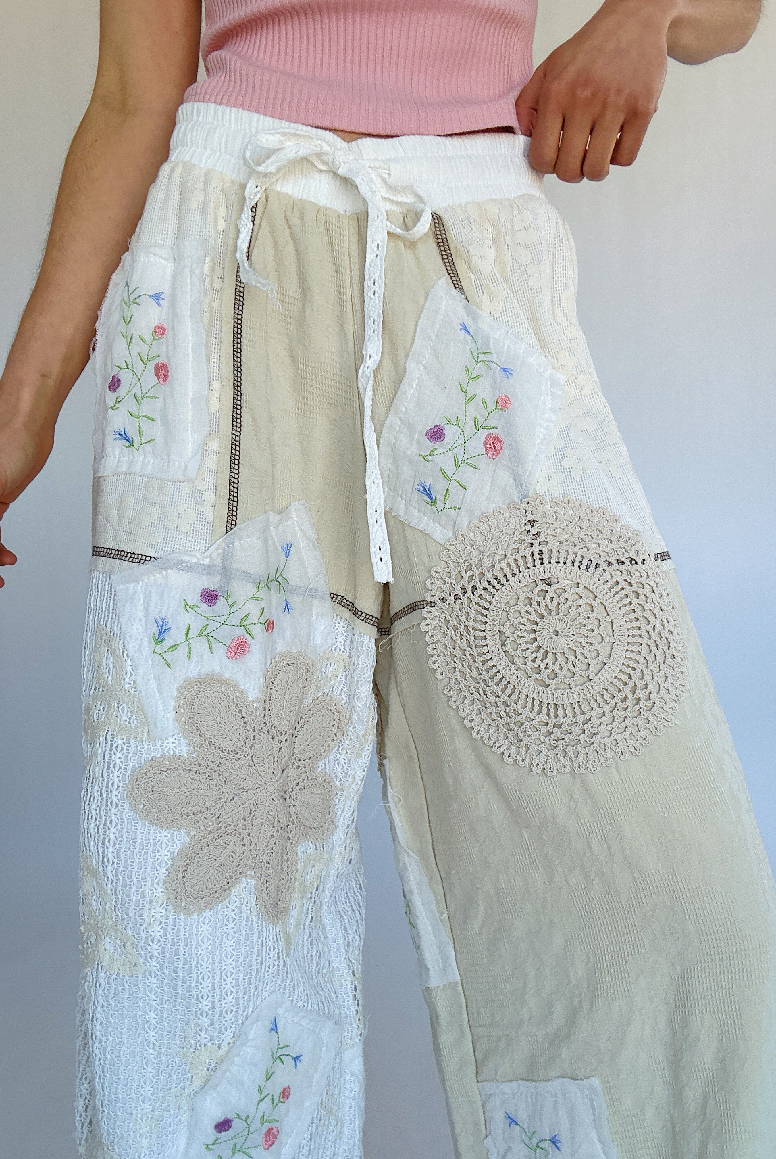 Person wearing a pair of wide-leg pants with floral and geometric embroidery on a plain background showing the elastic/drawstring waistband