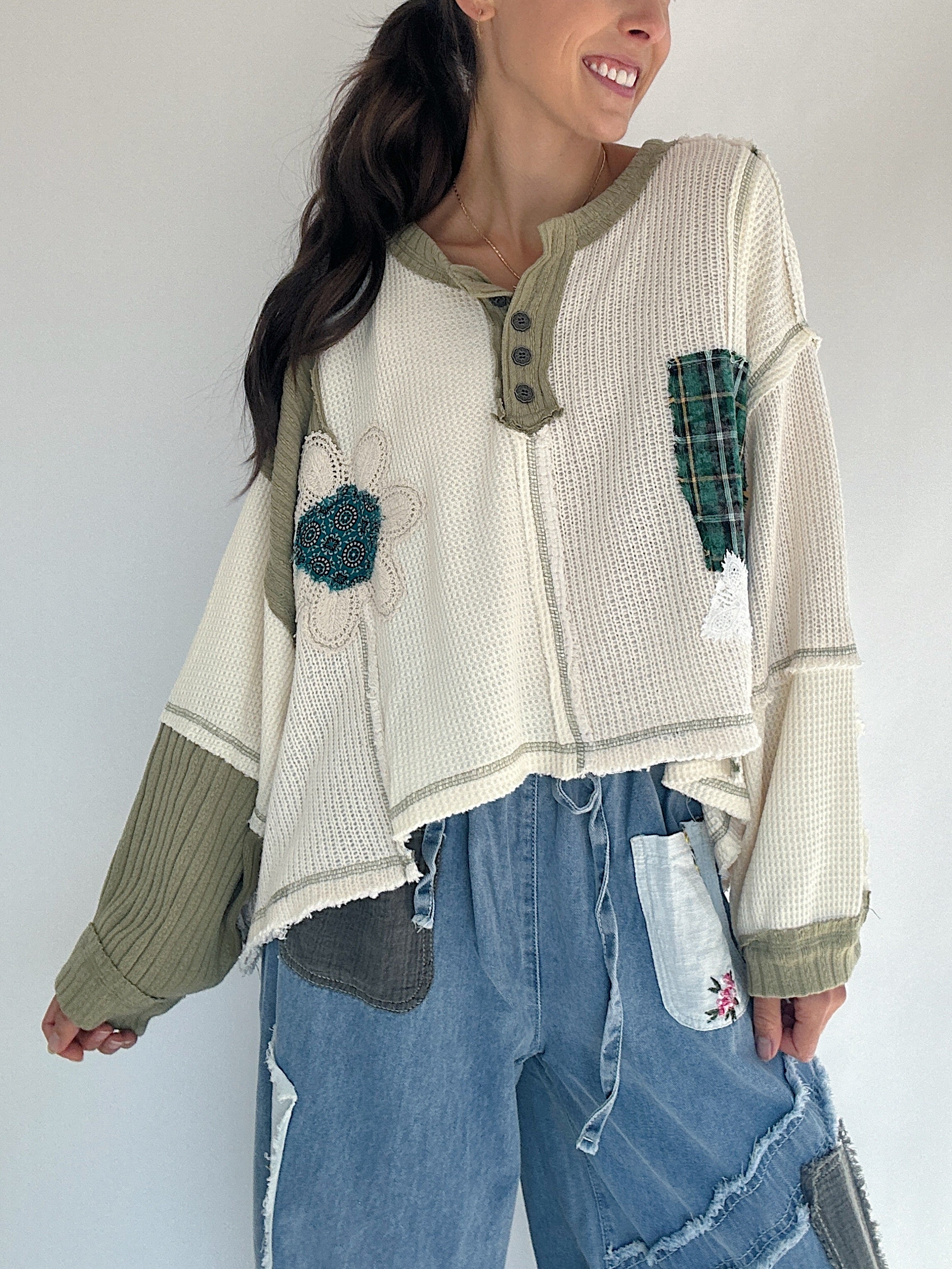 Woman wearing a textured sweater with floral and plaid designs against a plain background