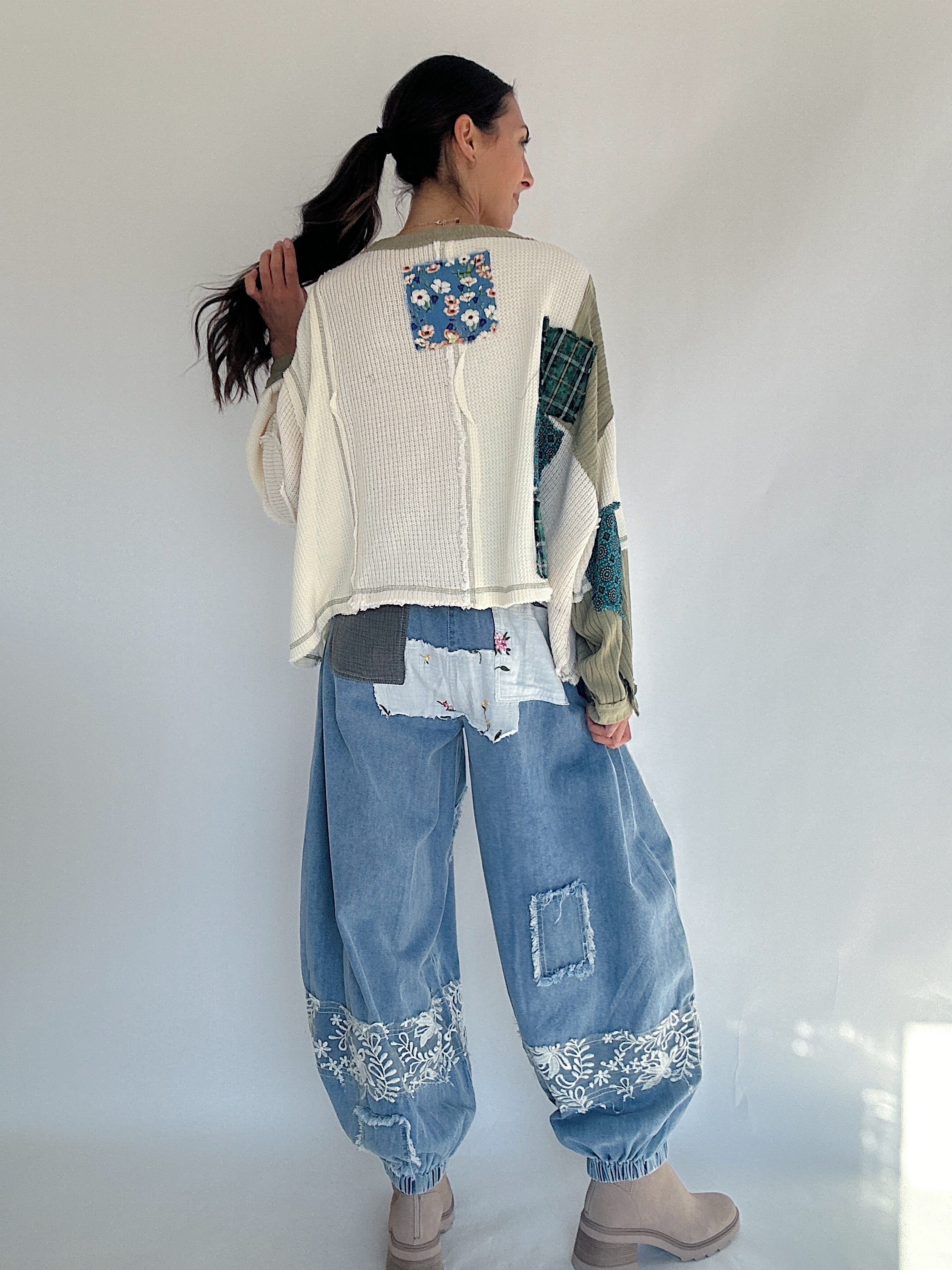 Person wearing a patchwork sweater and jeans against a white background to show the back view
