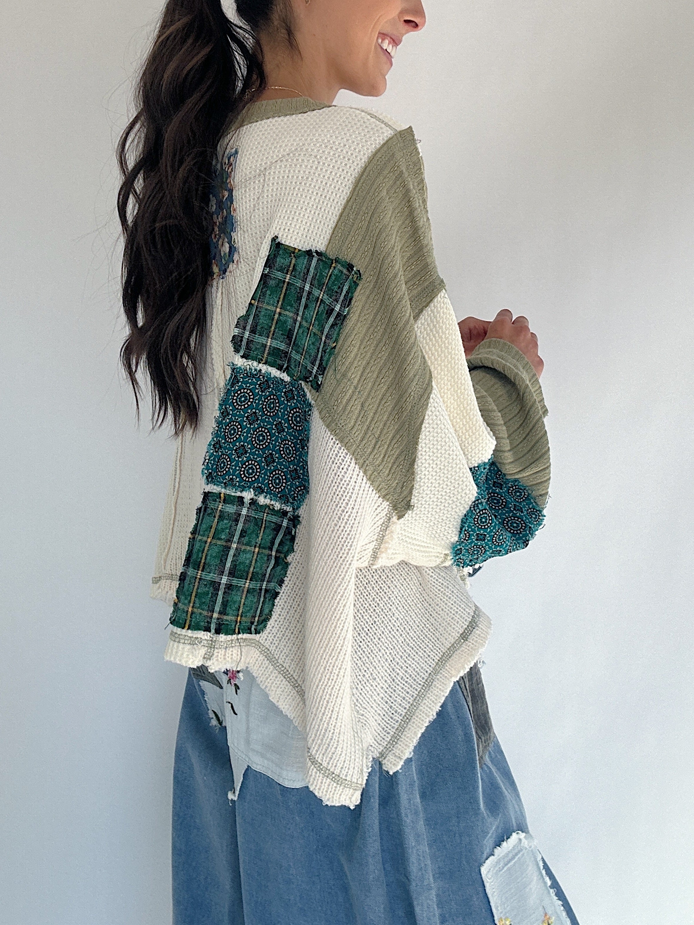 Person wearing a patchwork sweater with green and beige pattern against a white background showing back details