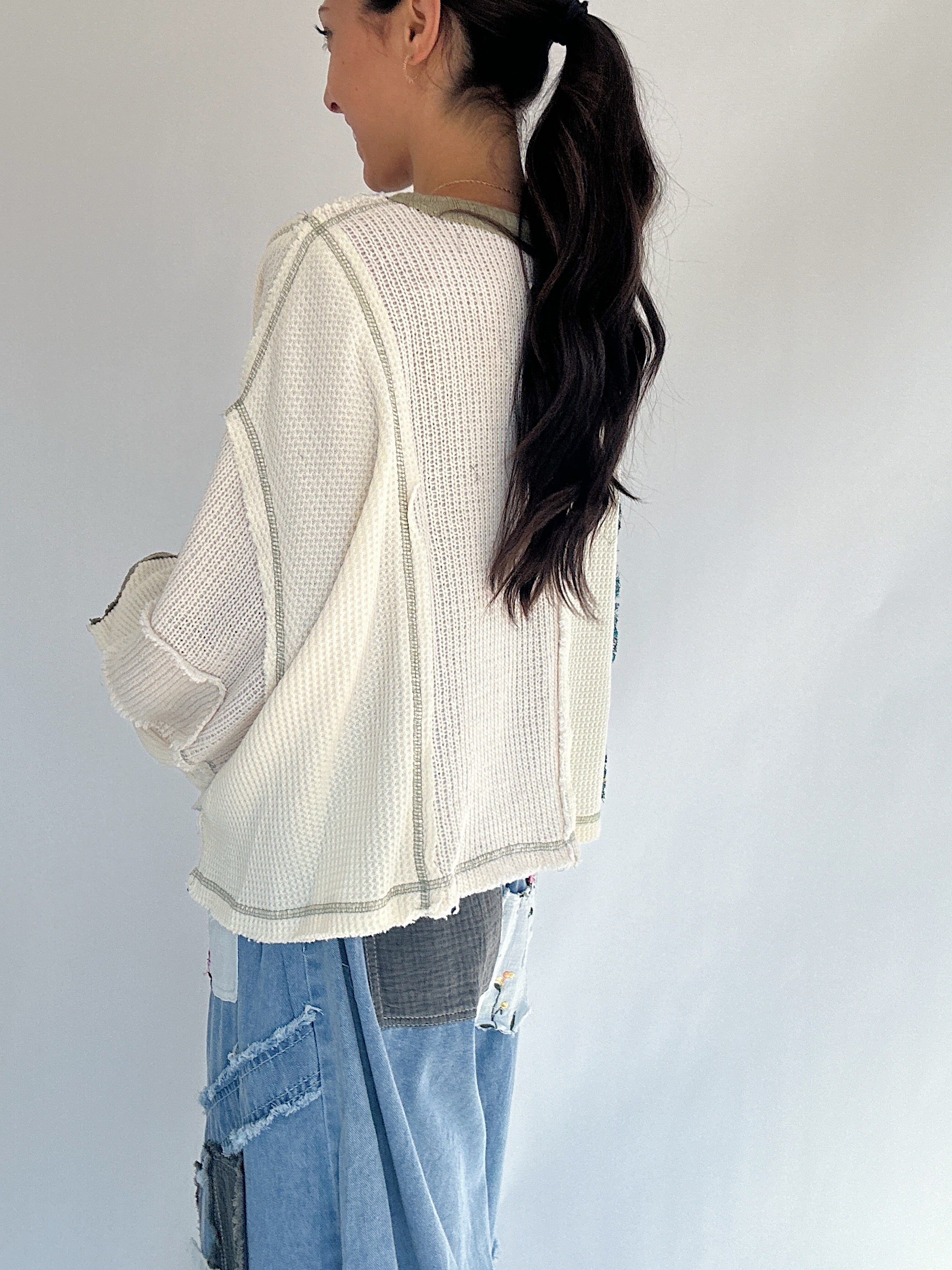 Person wearing a cream patchwork textured sweater and blue jeans against a plain background showing back detail