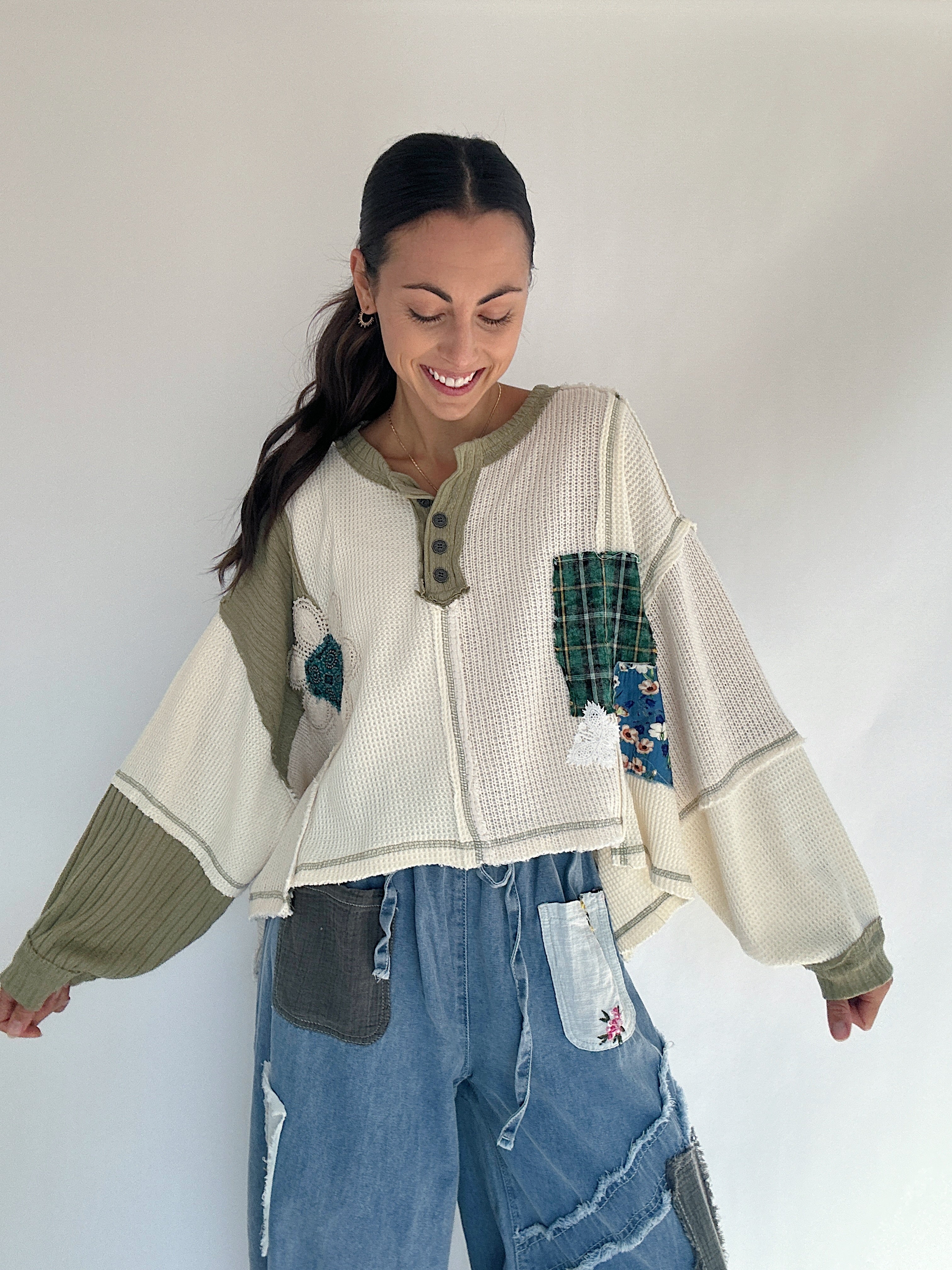 Woman wearing a patchwork sweater and jeans against a white background