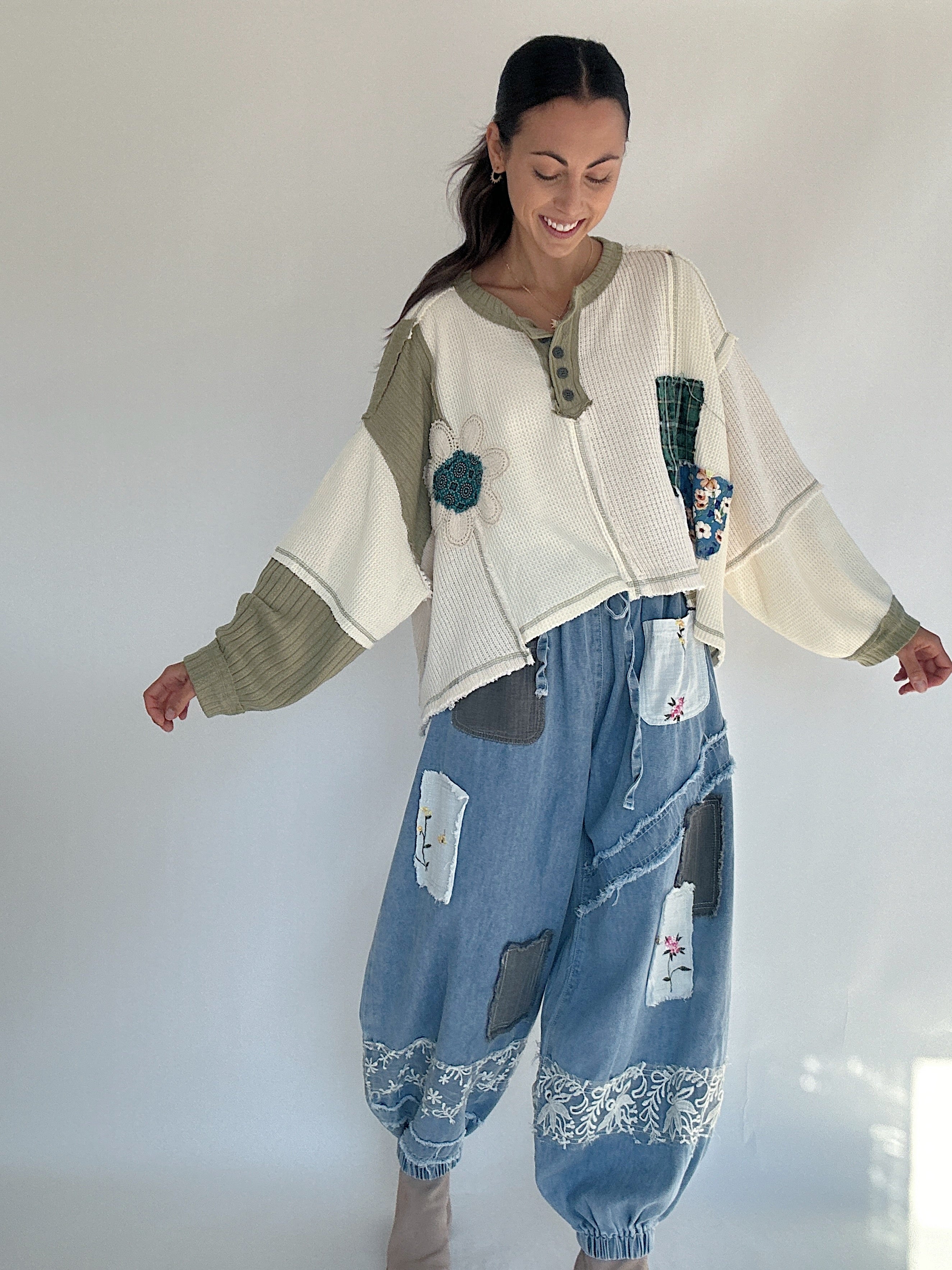 Woman wearing a patchwork outfit with a cream knit top and blue jeans against a plain background