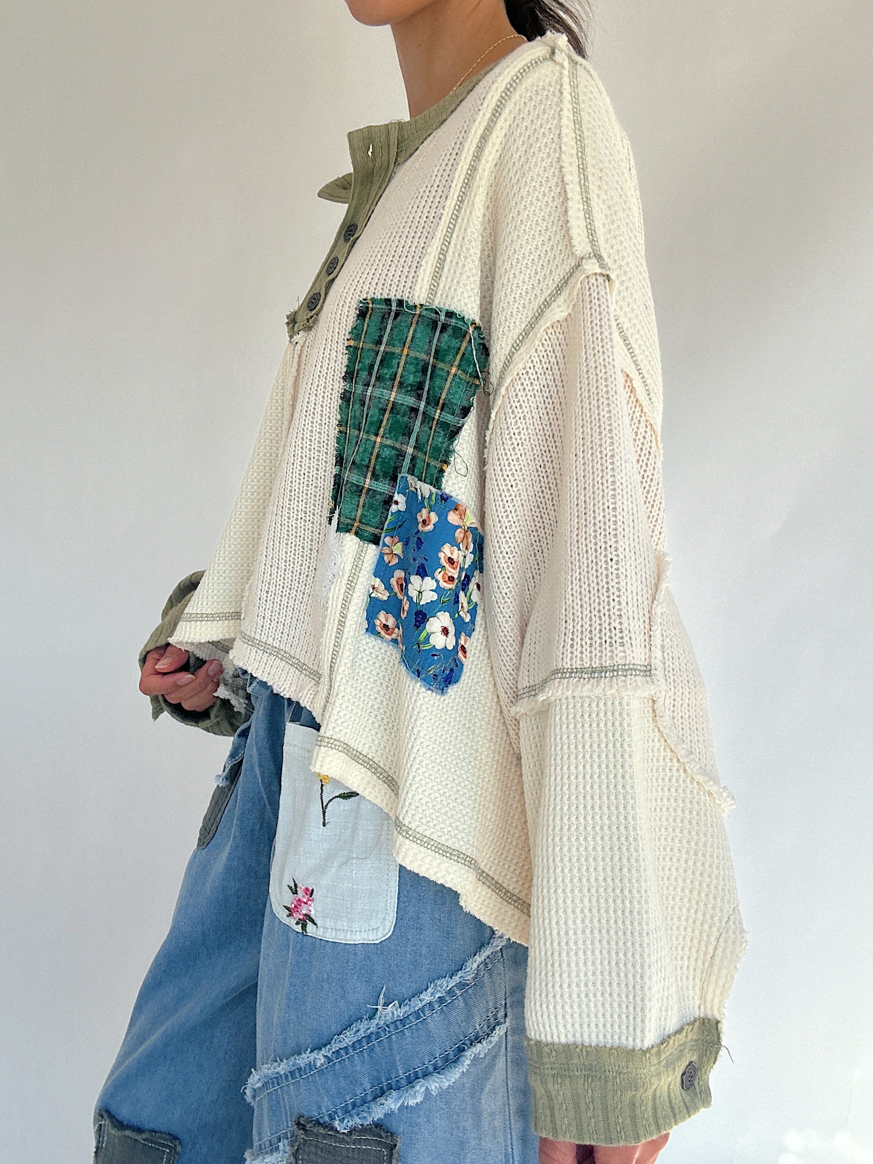 Person wearing a patchwork knit top with floral and plaid pattern patches on a plain background showing side view