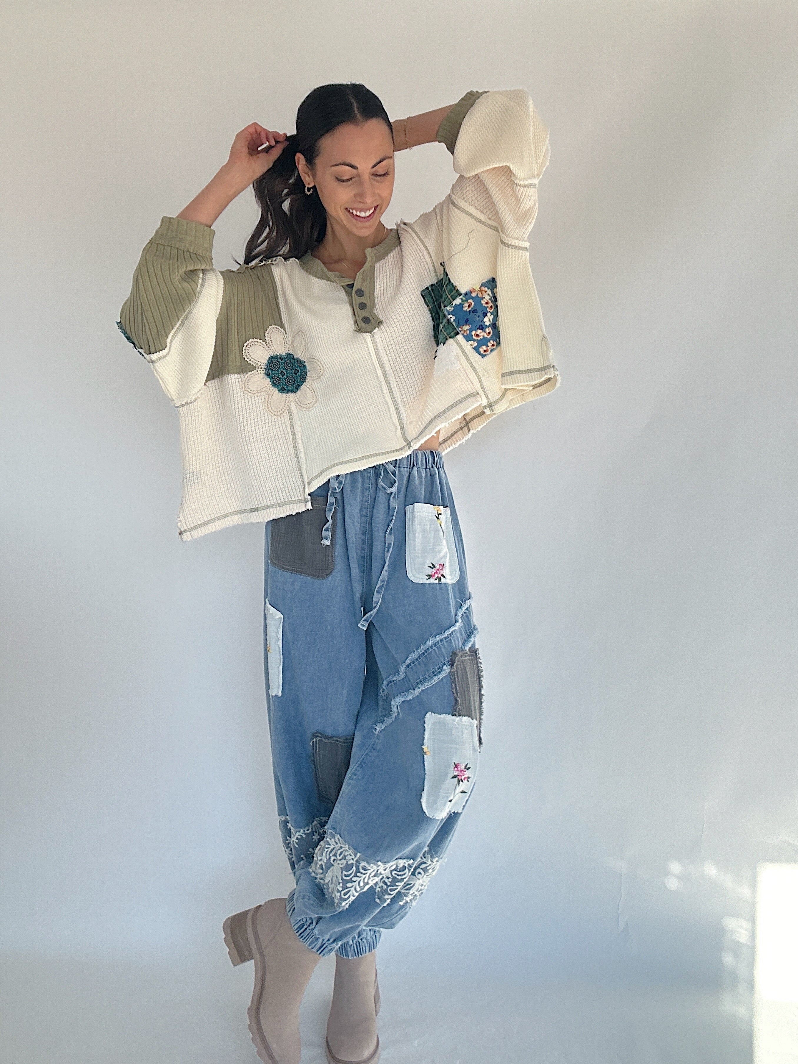 Person wearing a patchwork outfit with a cream knit top and blue jeans against a plain background