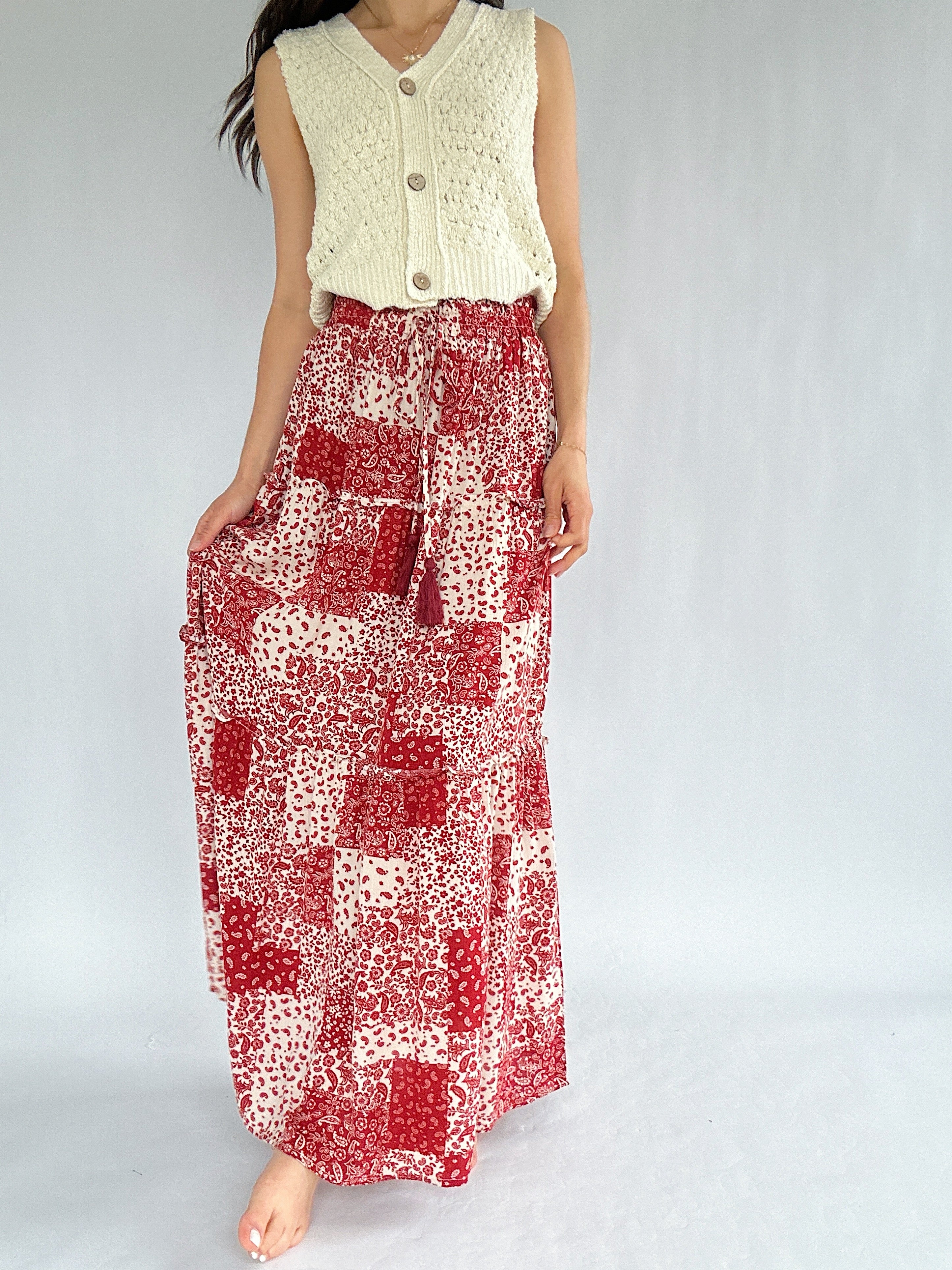 Person wearing a long red and white patterned skirt with a light-colored top on a plain background