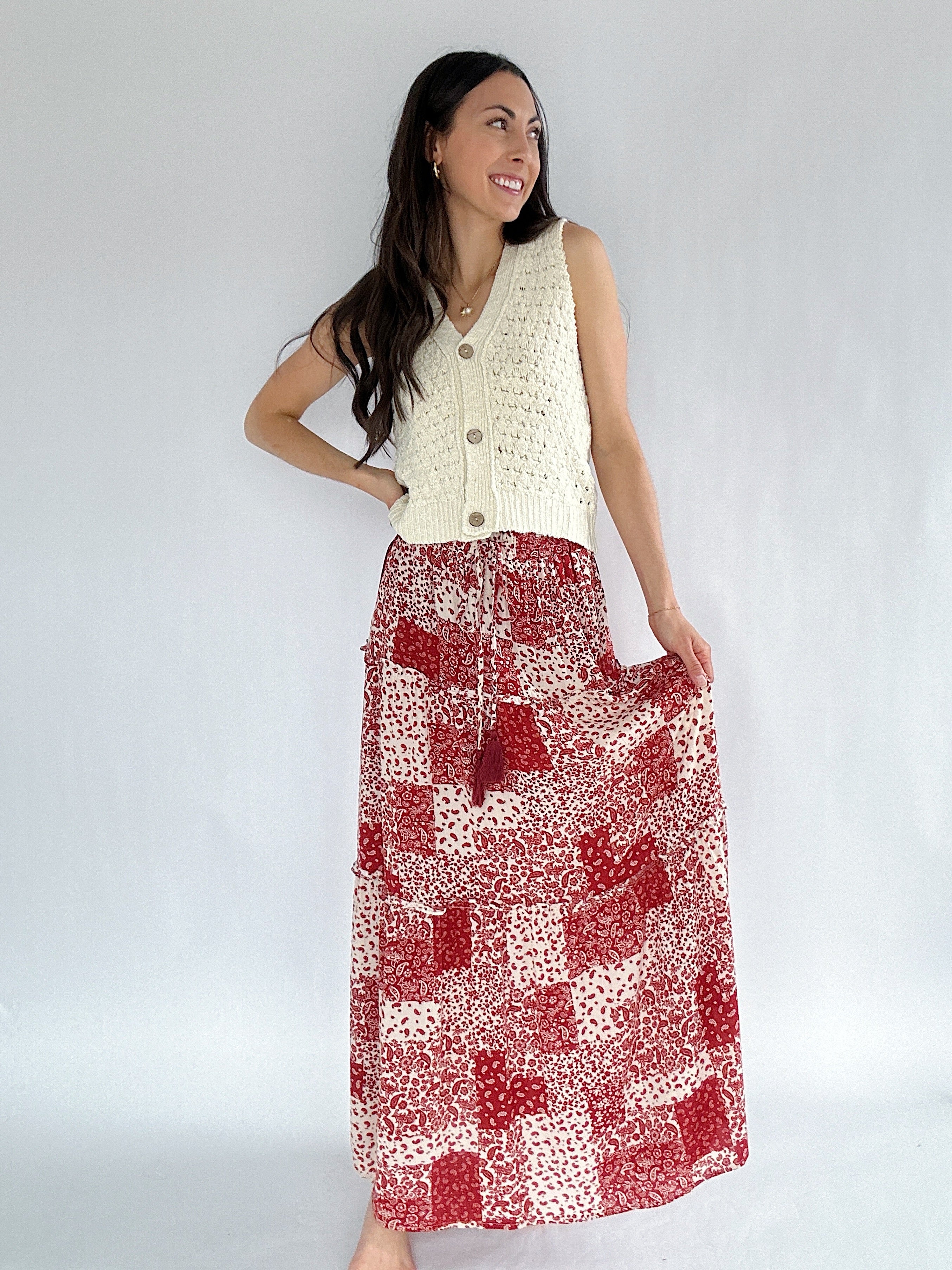 Woman wearing a white sleeveless top and red patterned skirt against a plain background