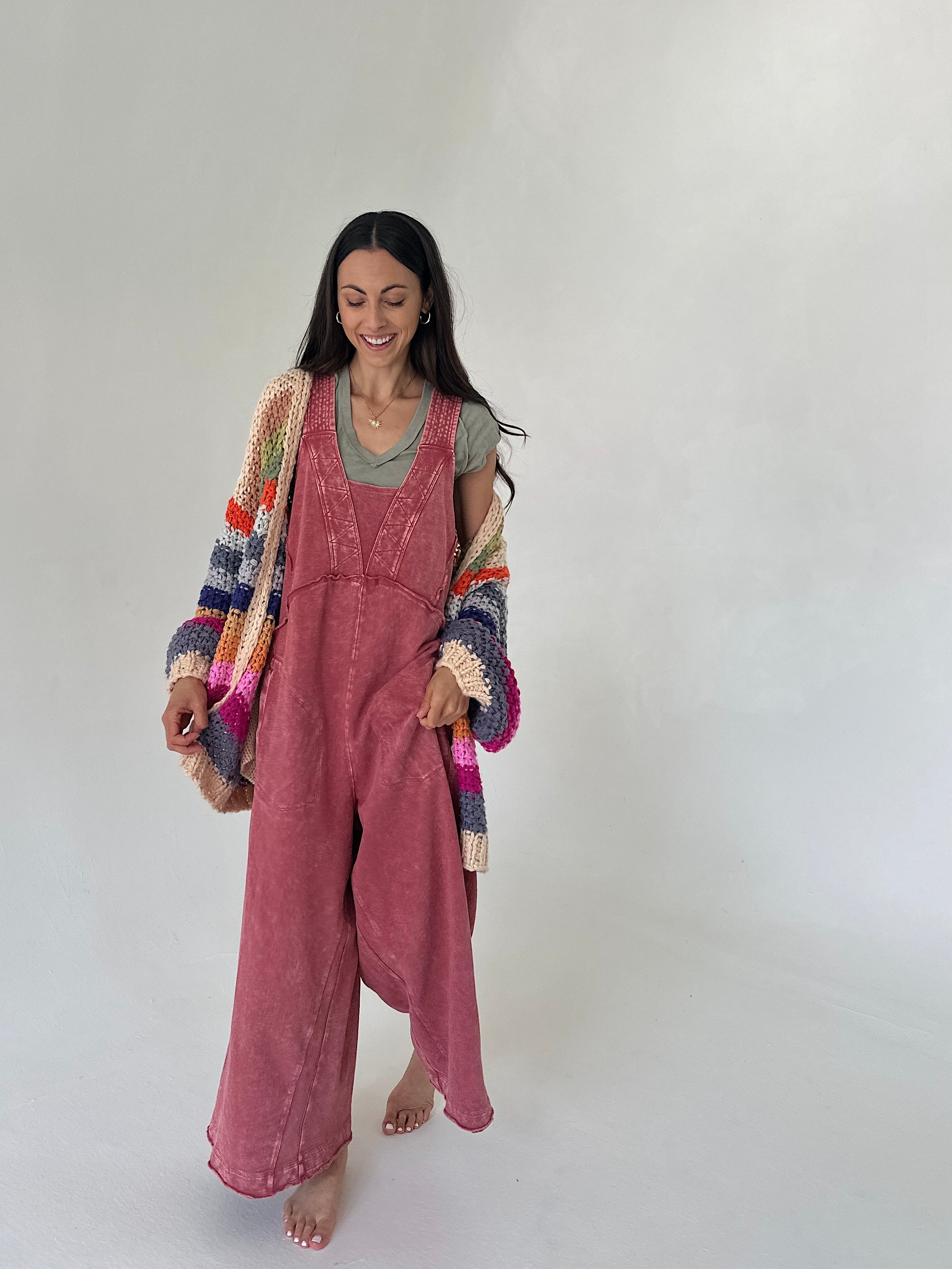 Woman wearing pink terry knit overalls with a colorful cardigan on a white background