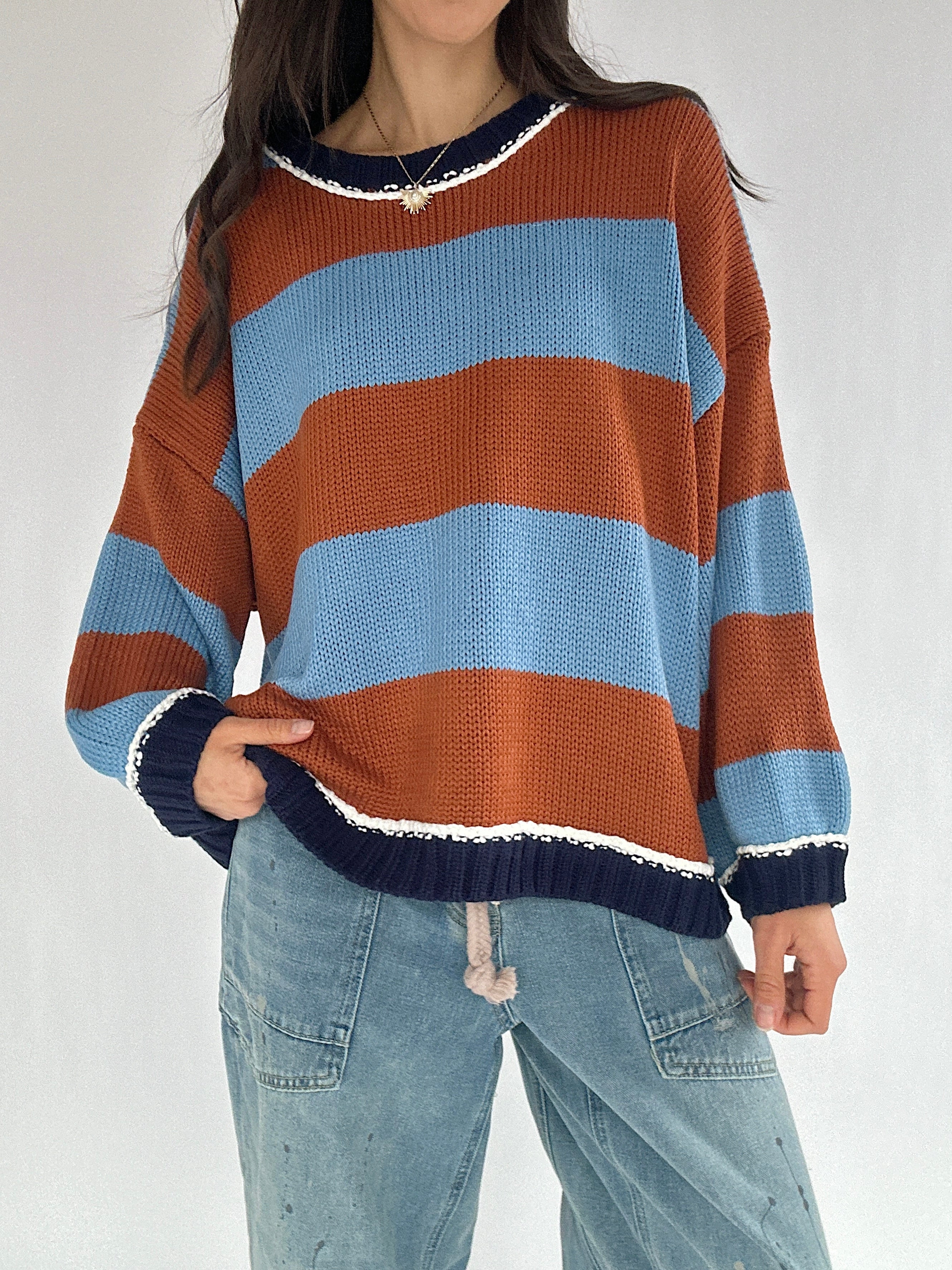 Person wearing a striped sweater with brown, blue, and navy colors on a white background