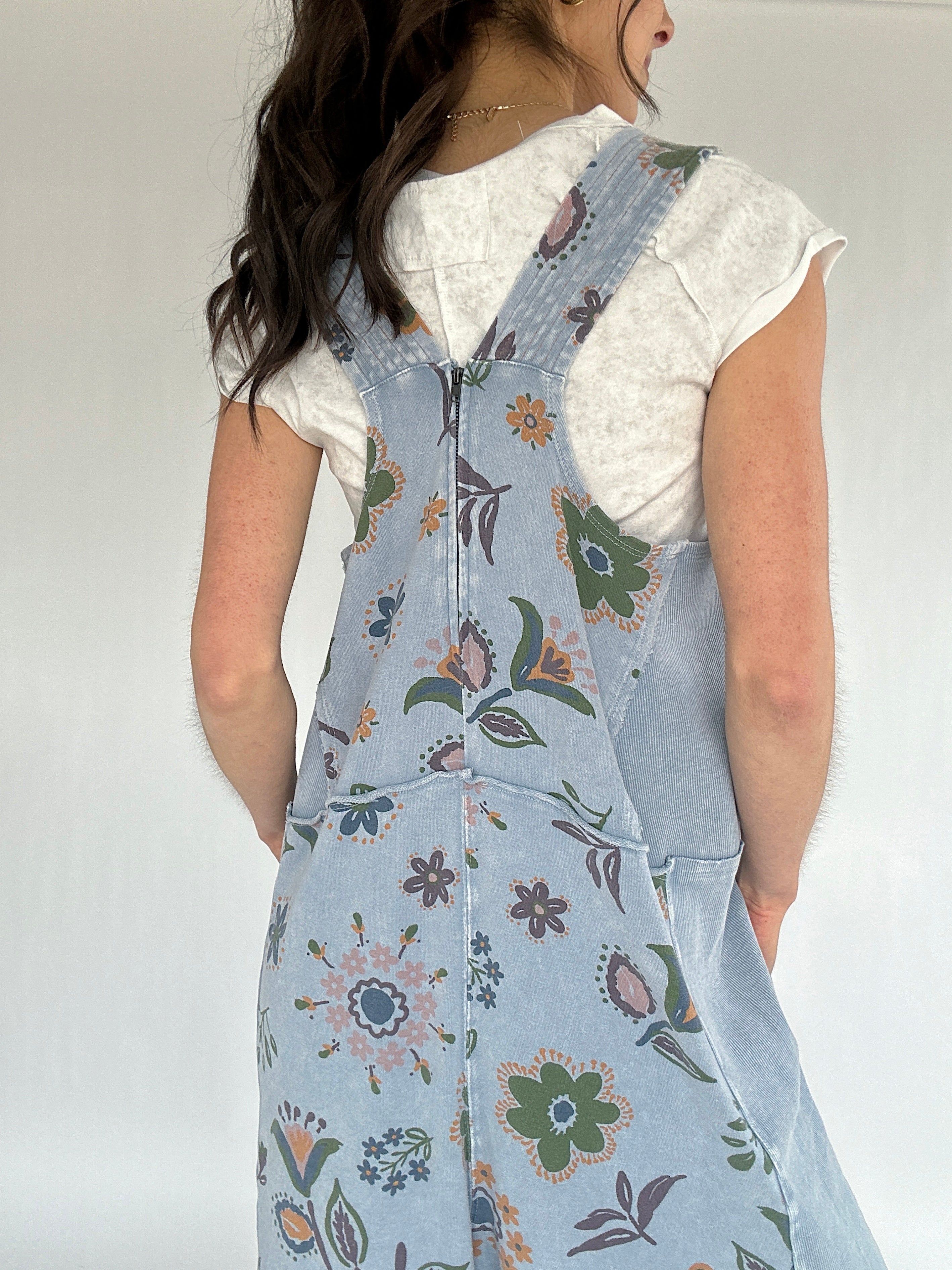 Person wearing a floral blue jumpsuit over a white top against a plain background showing the back zipper detail