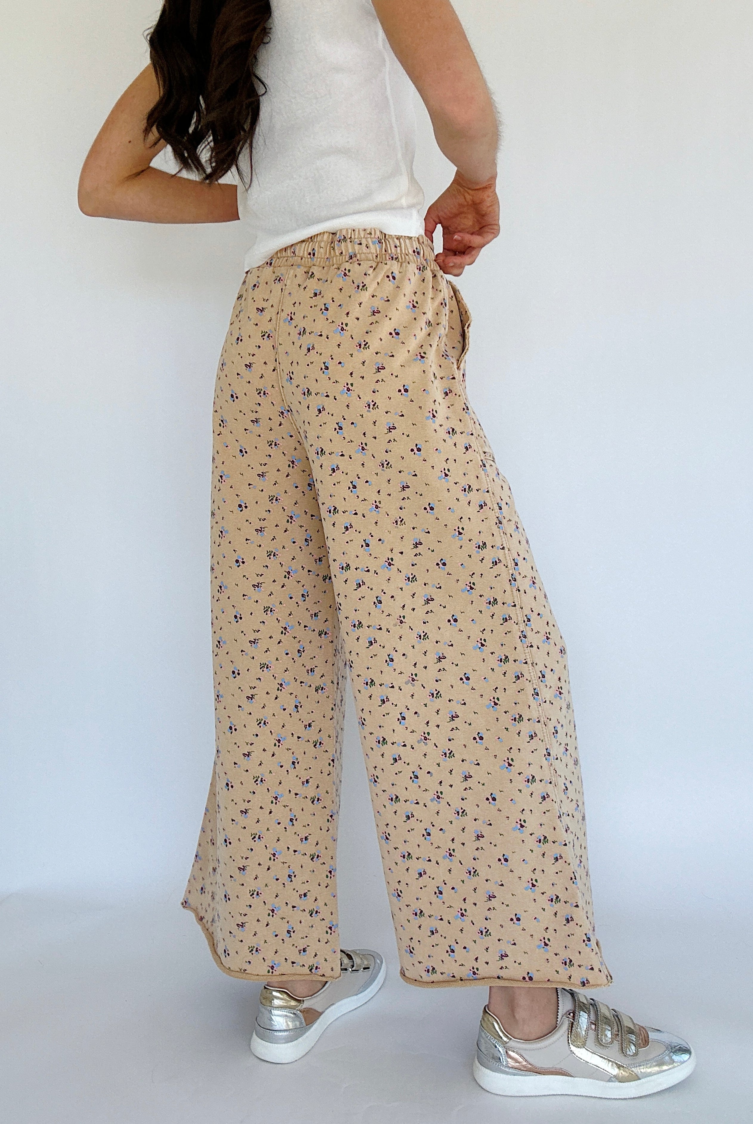Person wearing beige floral pants and white sneakers on a plain background