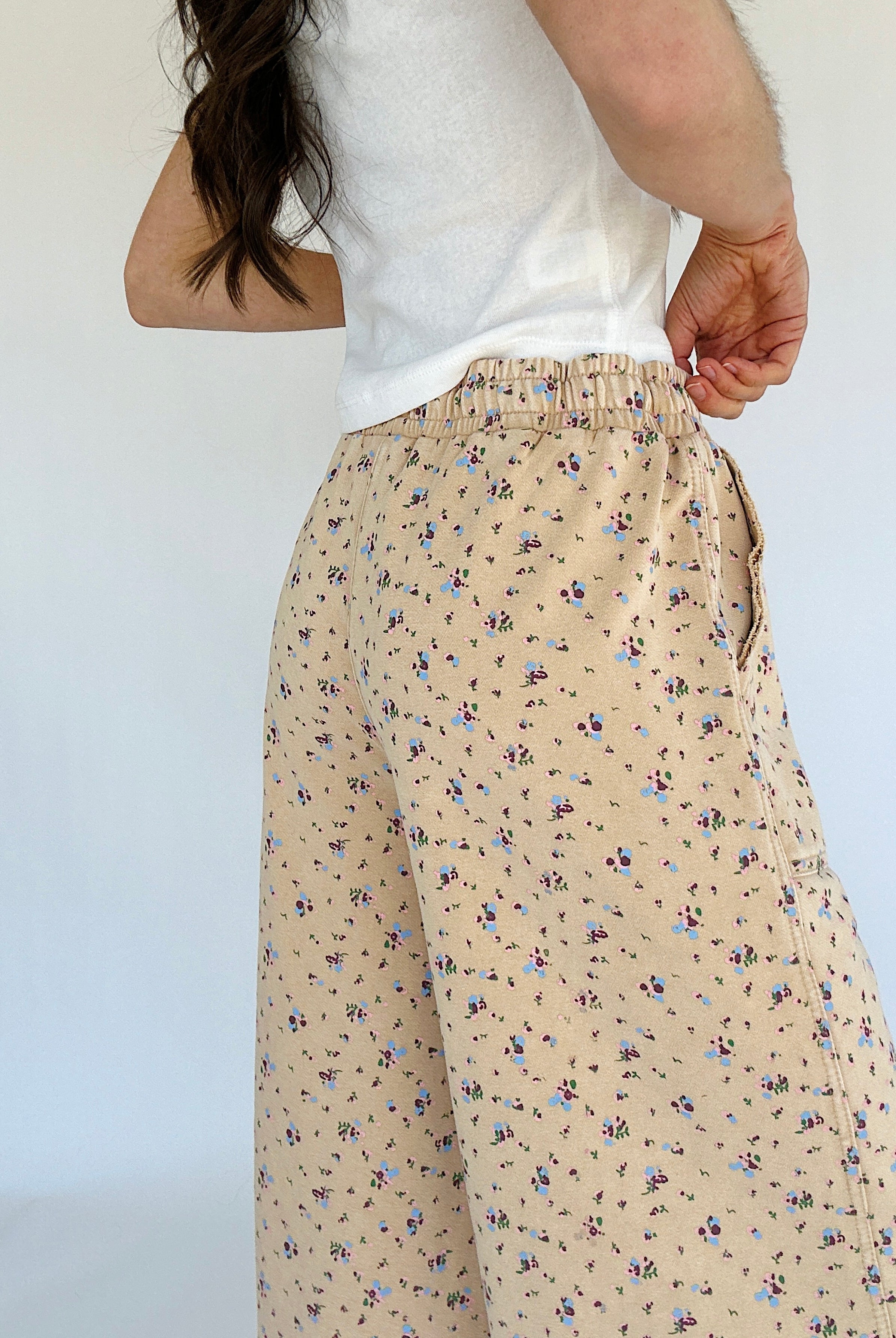 Person wearing beige floral pants with a white top against a plain background