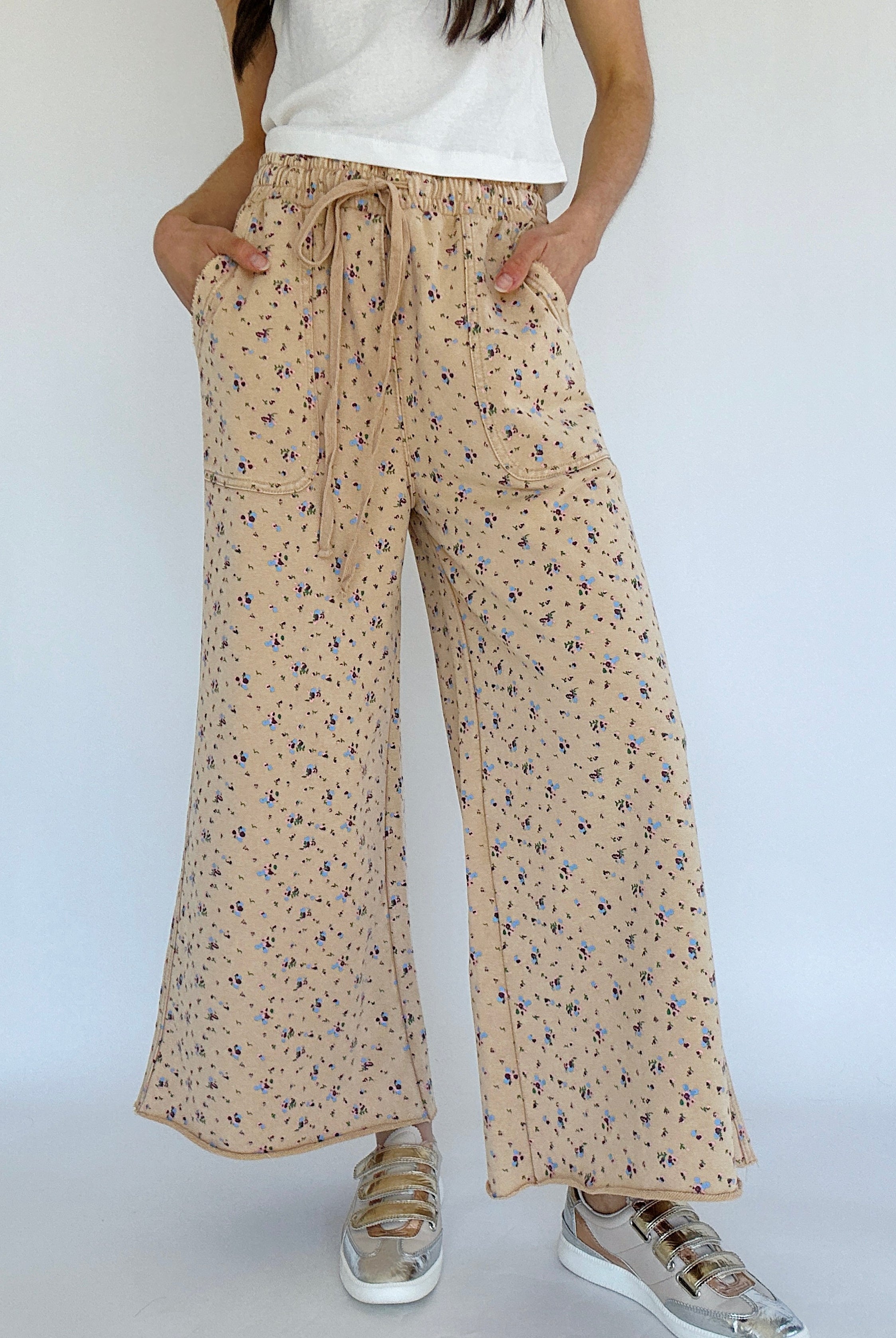 Person wearing beige floral wide-leg pants on a white background