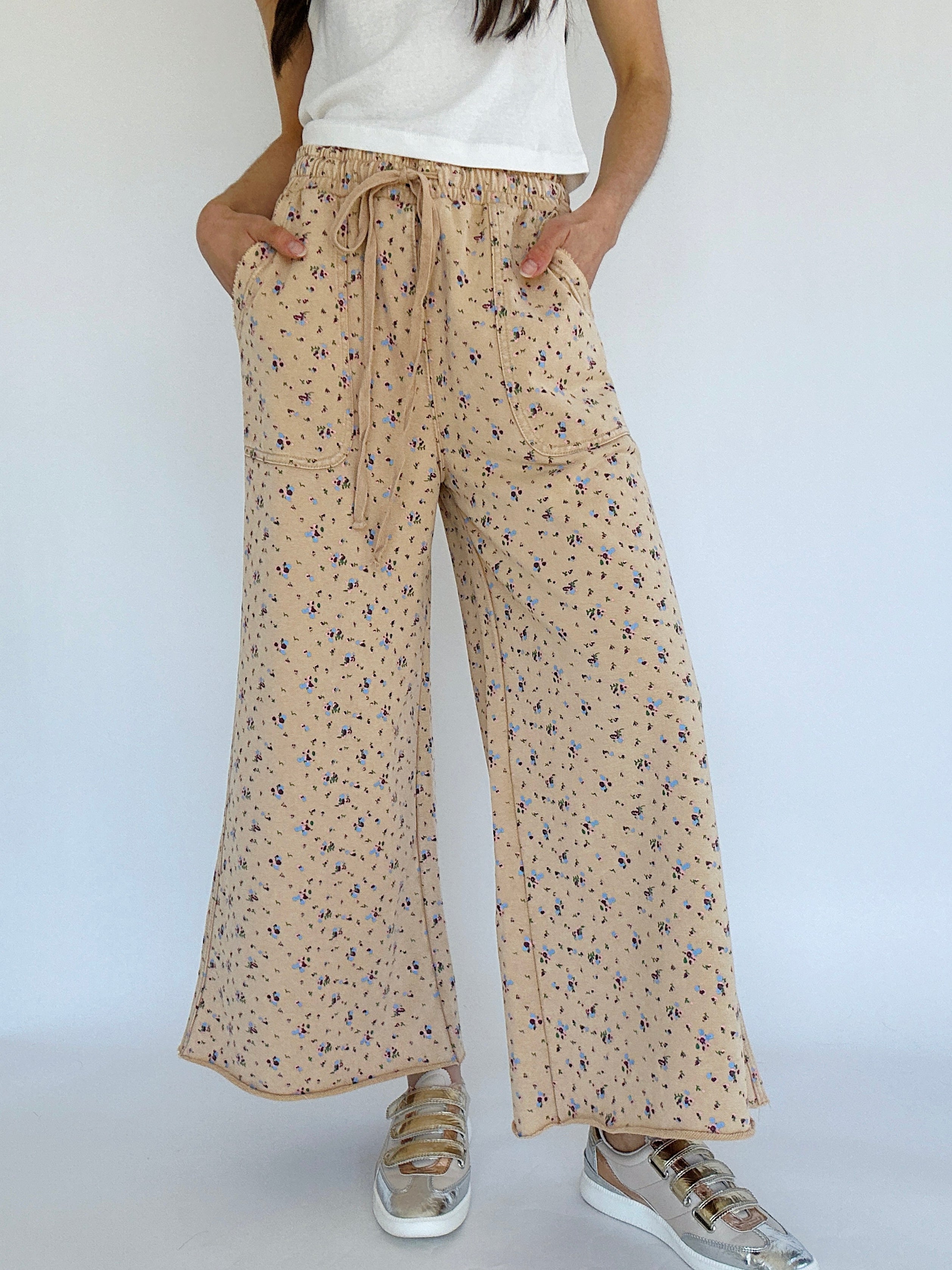 Person wearing beige floral wide-leg pants on a white background
