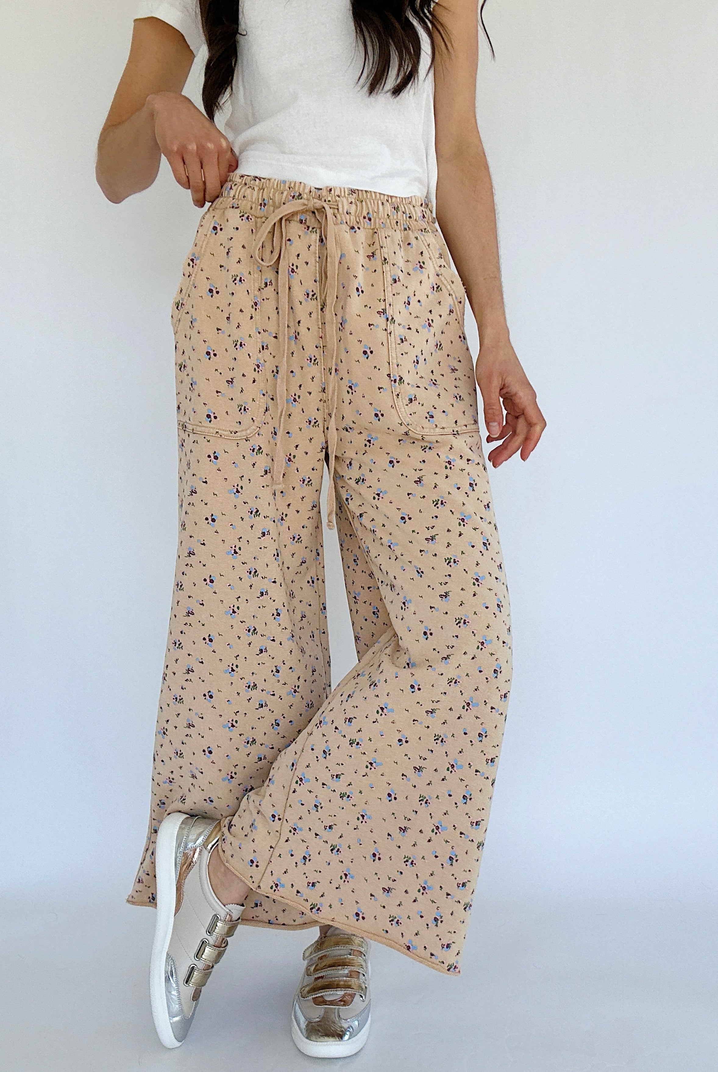 Person wearing beige floral wide-leg pants with a white top on a plain background