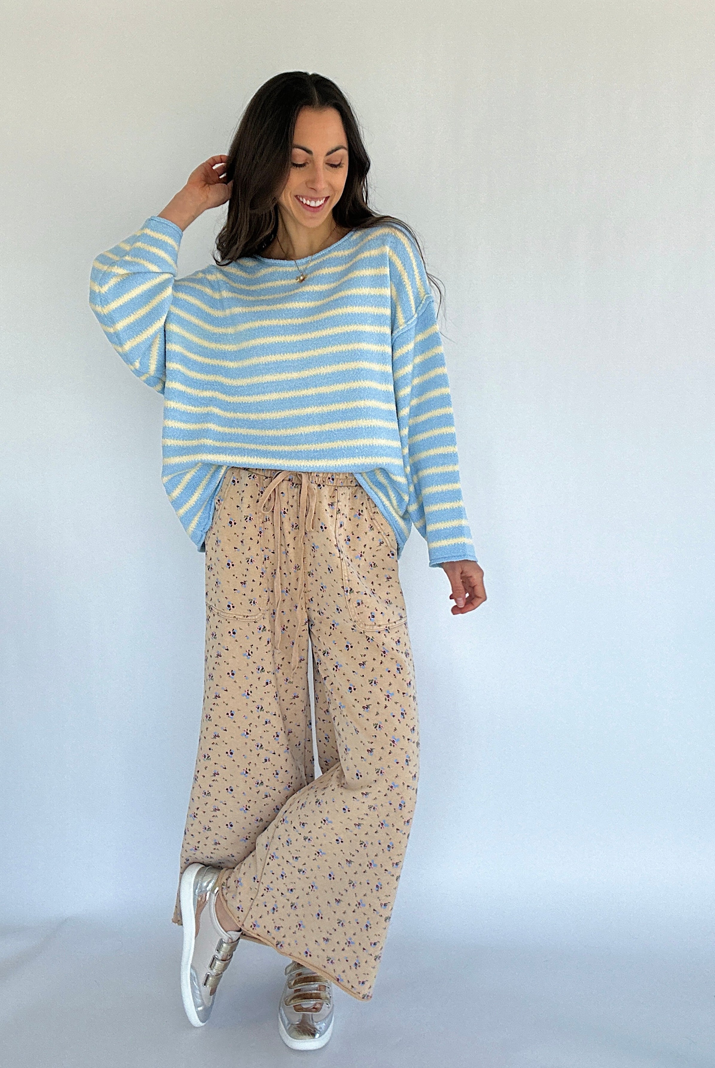 Woman wearing a striped sweater and floral patterned pants against a white background