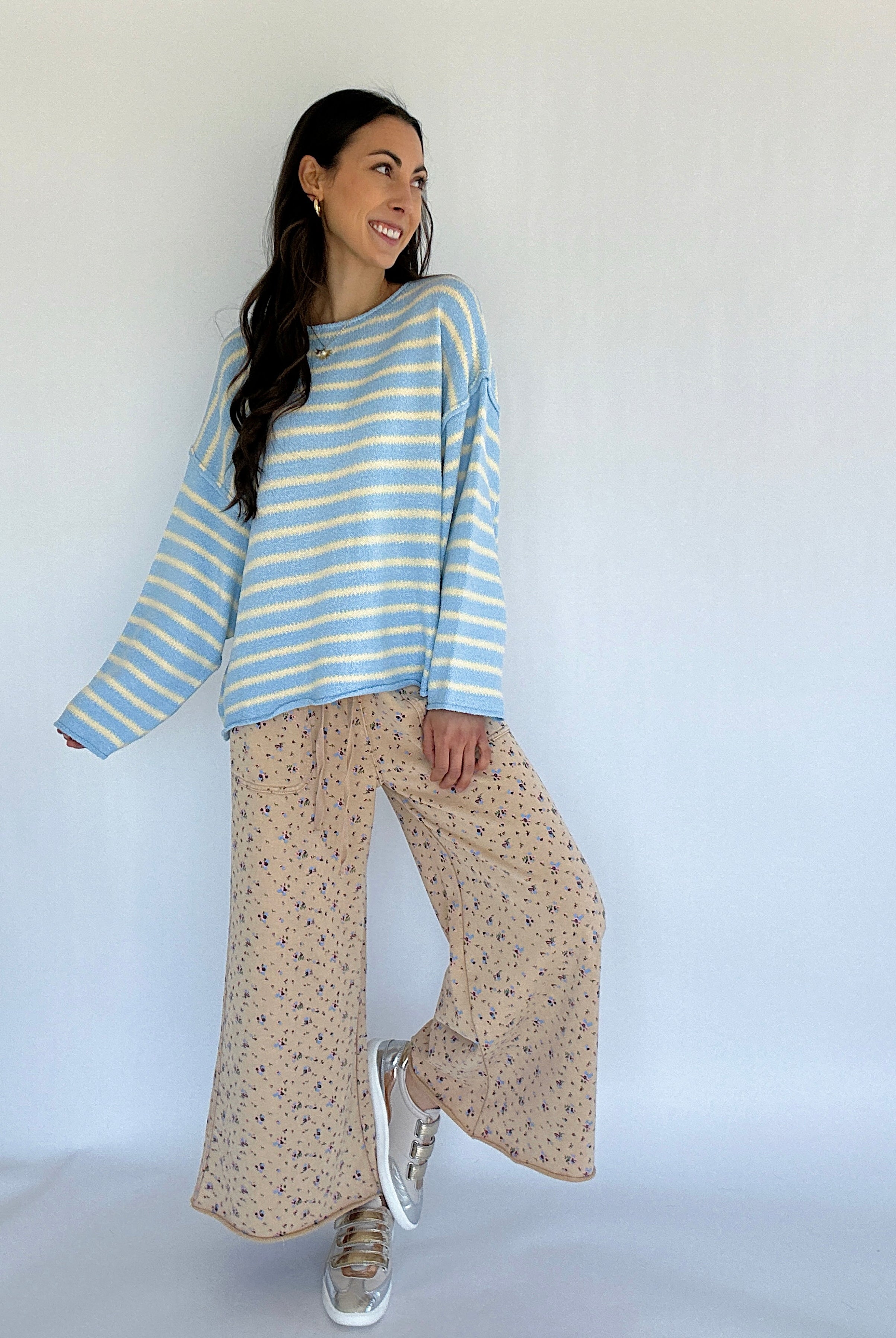 Woman wearing a blue and white striped sweater and beige patterned pants against a white background