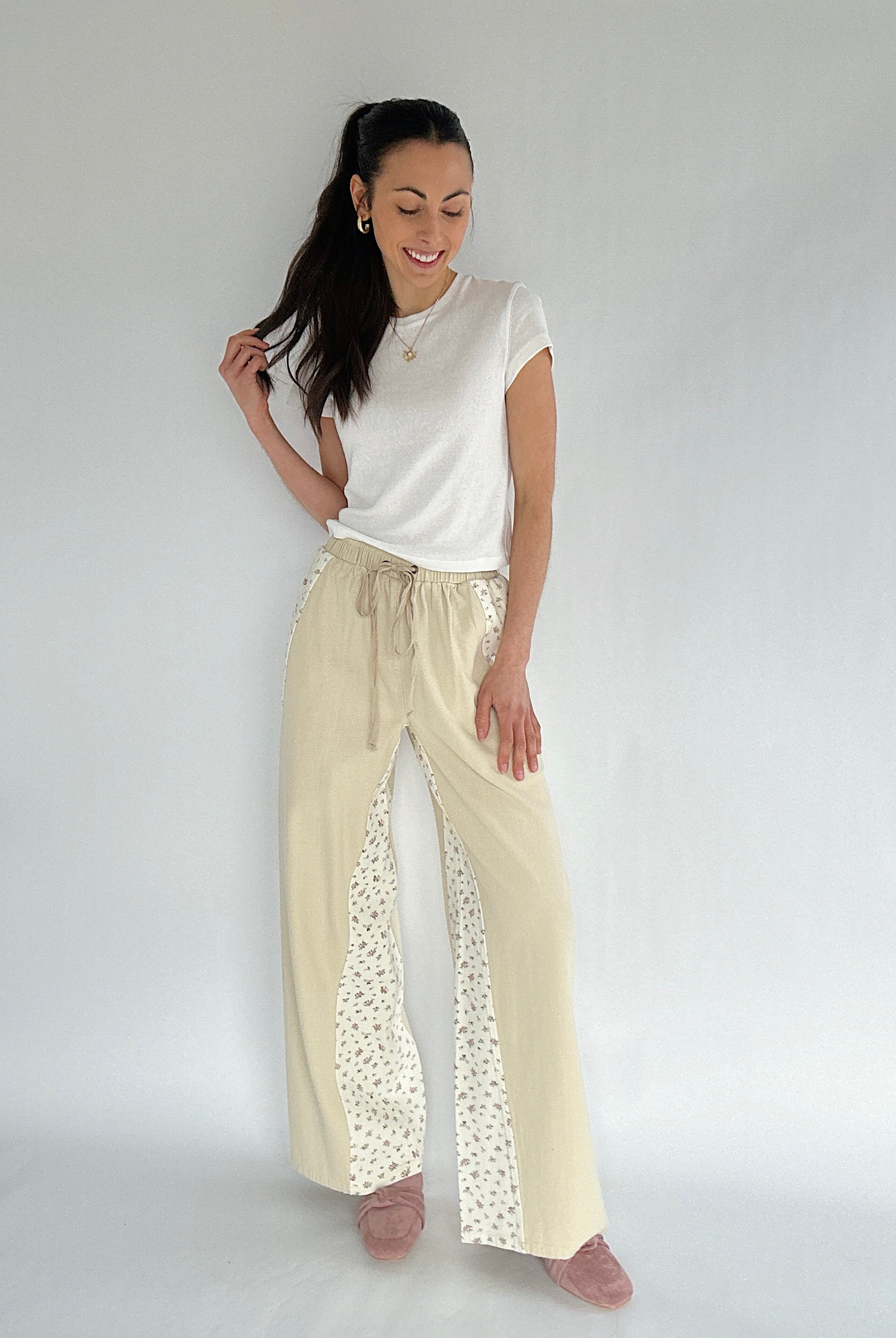 Woman wearing a white top and beige pants with floral accents on a plain background