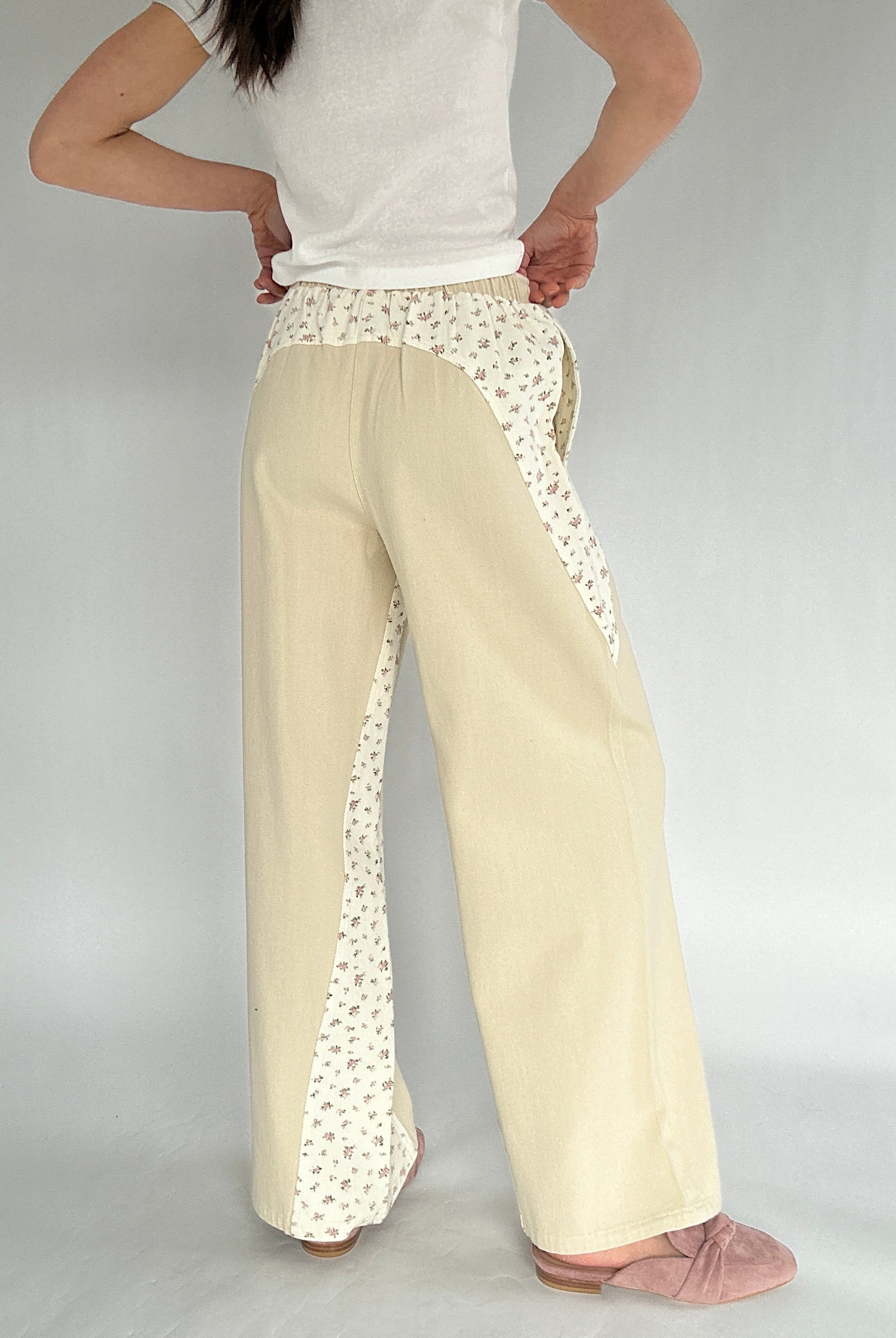 Beige pants with floral detailing worn by a person on a plain background showing back