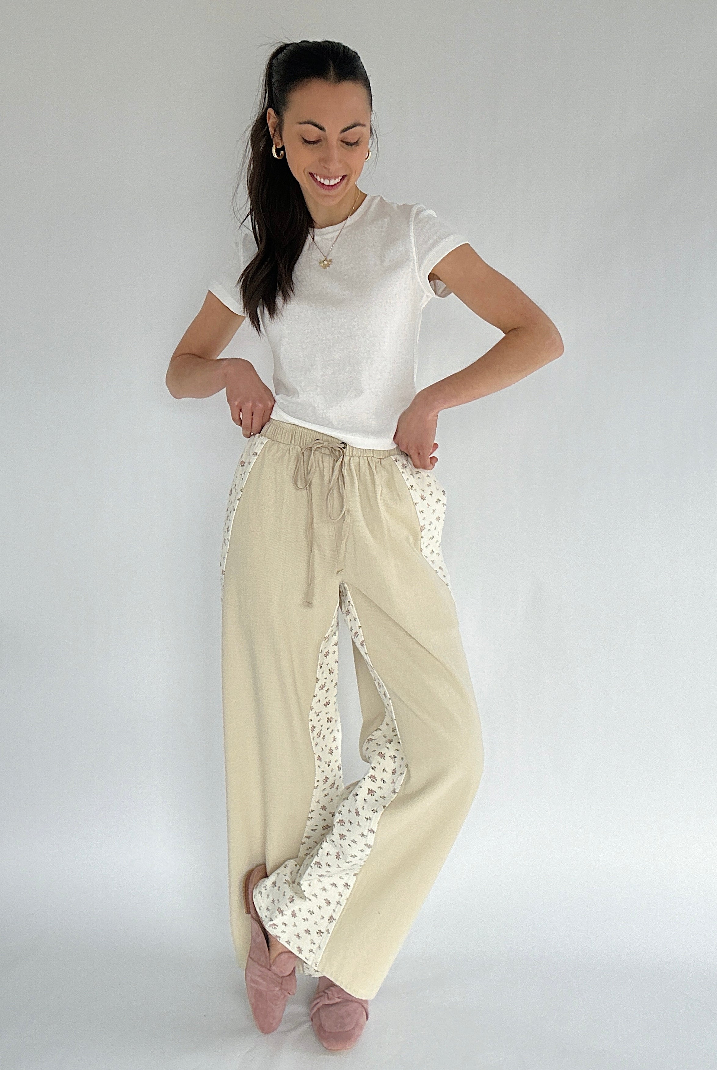 Woman wearing a white top and beige pants with floral accents on a plain background