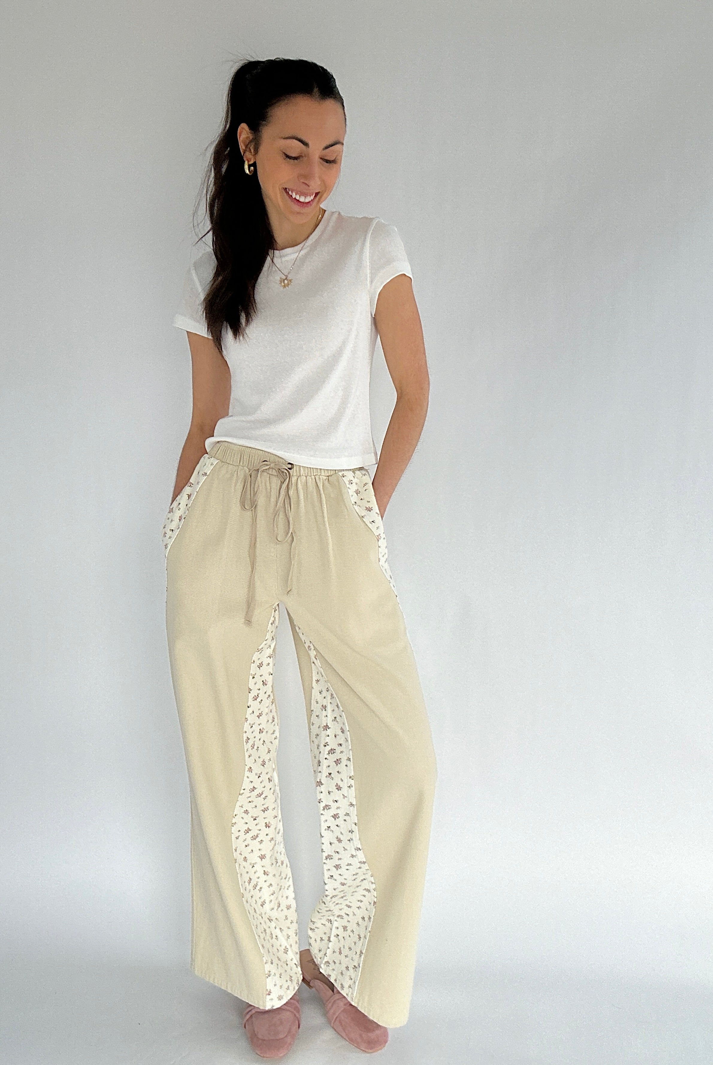 Woman wearing a white top and beige pants with floral accents on a plain background