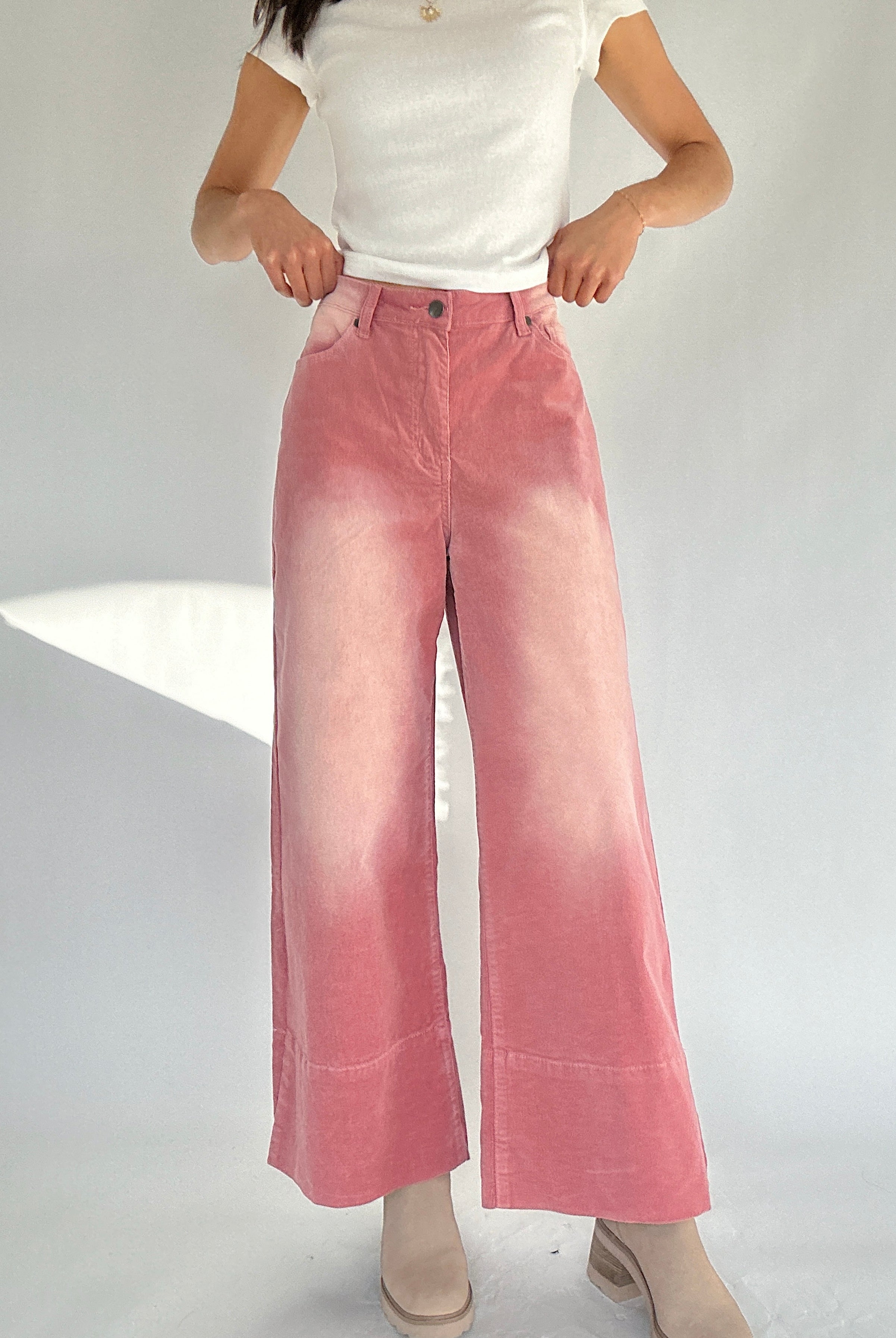 Person wearing pink corduroy wide-leg pants and a white top on a plain background
