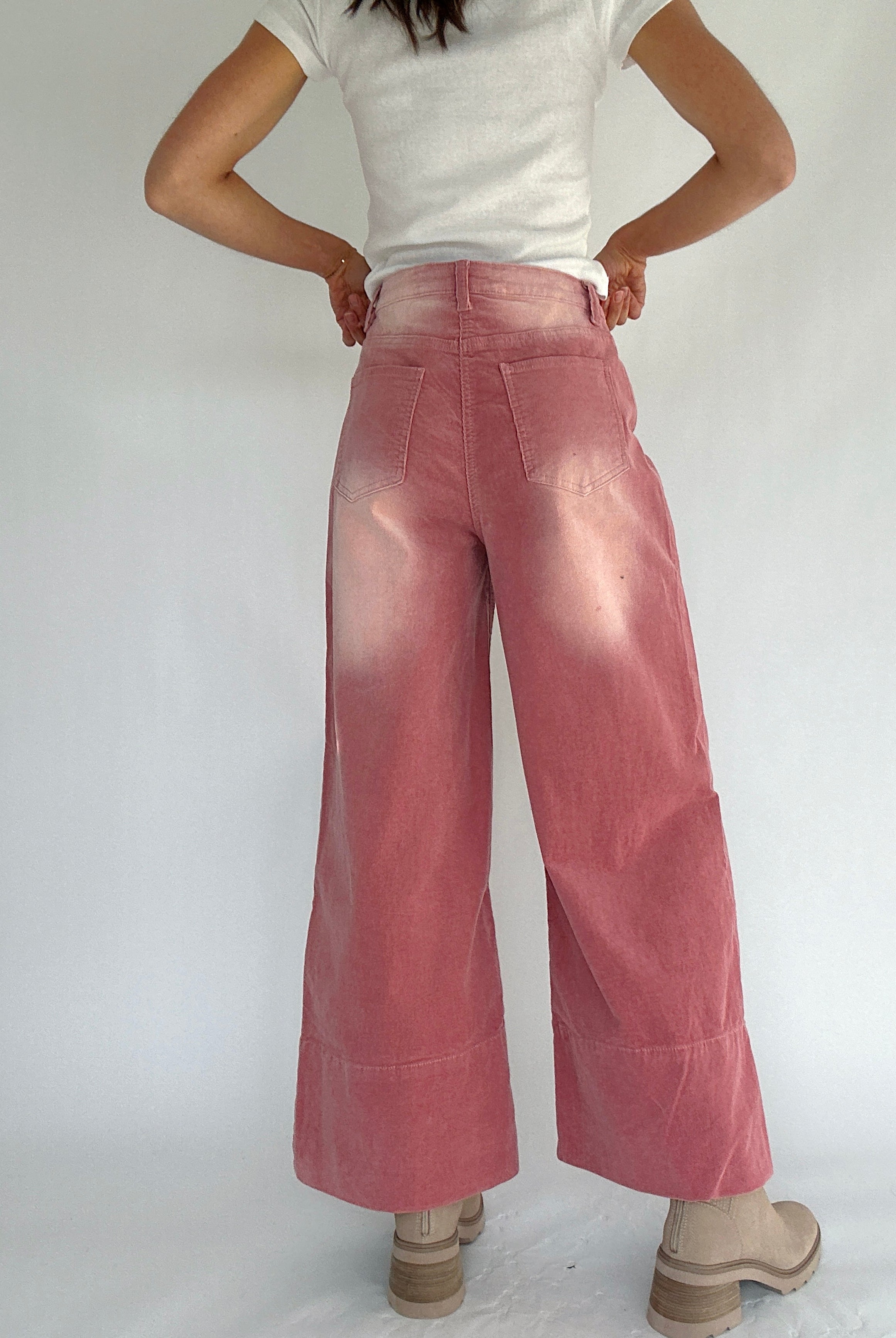 Person wearing pink corduroy wide-leg pants and a white top on a plain background