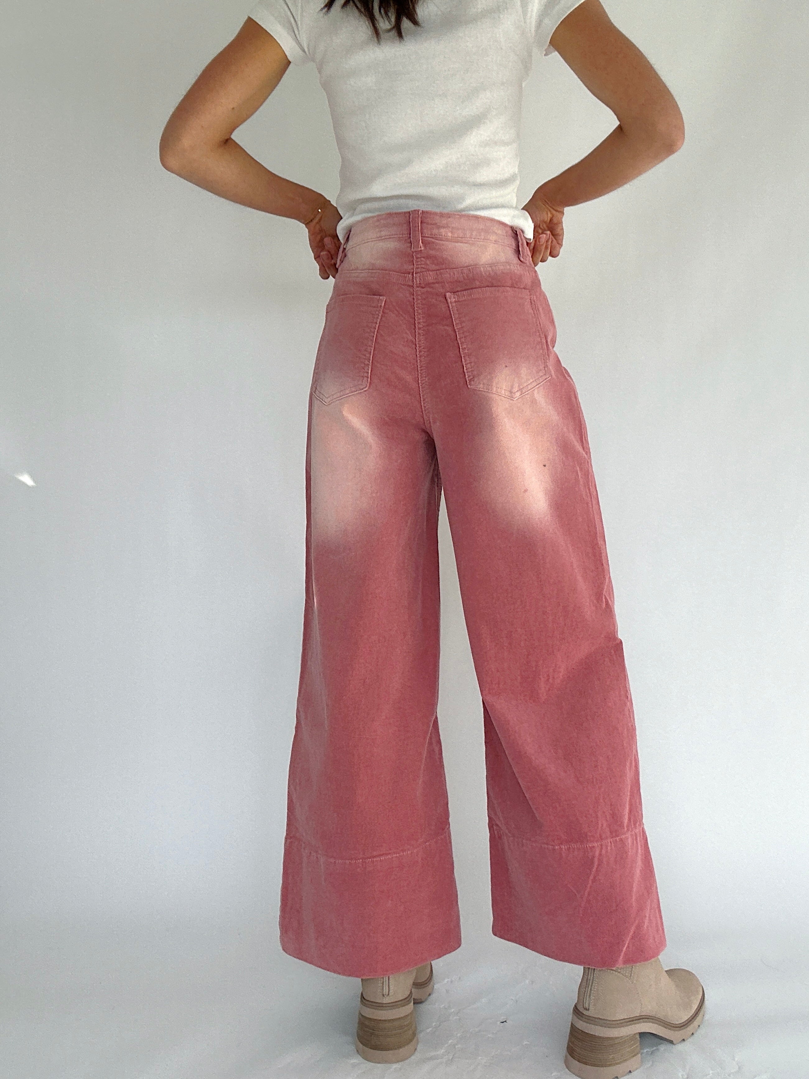 Person wearing pink corduroy wide-leg pants and a white top on a plain background