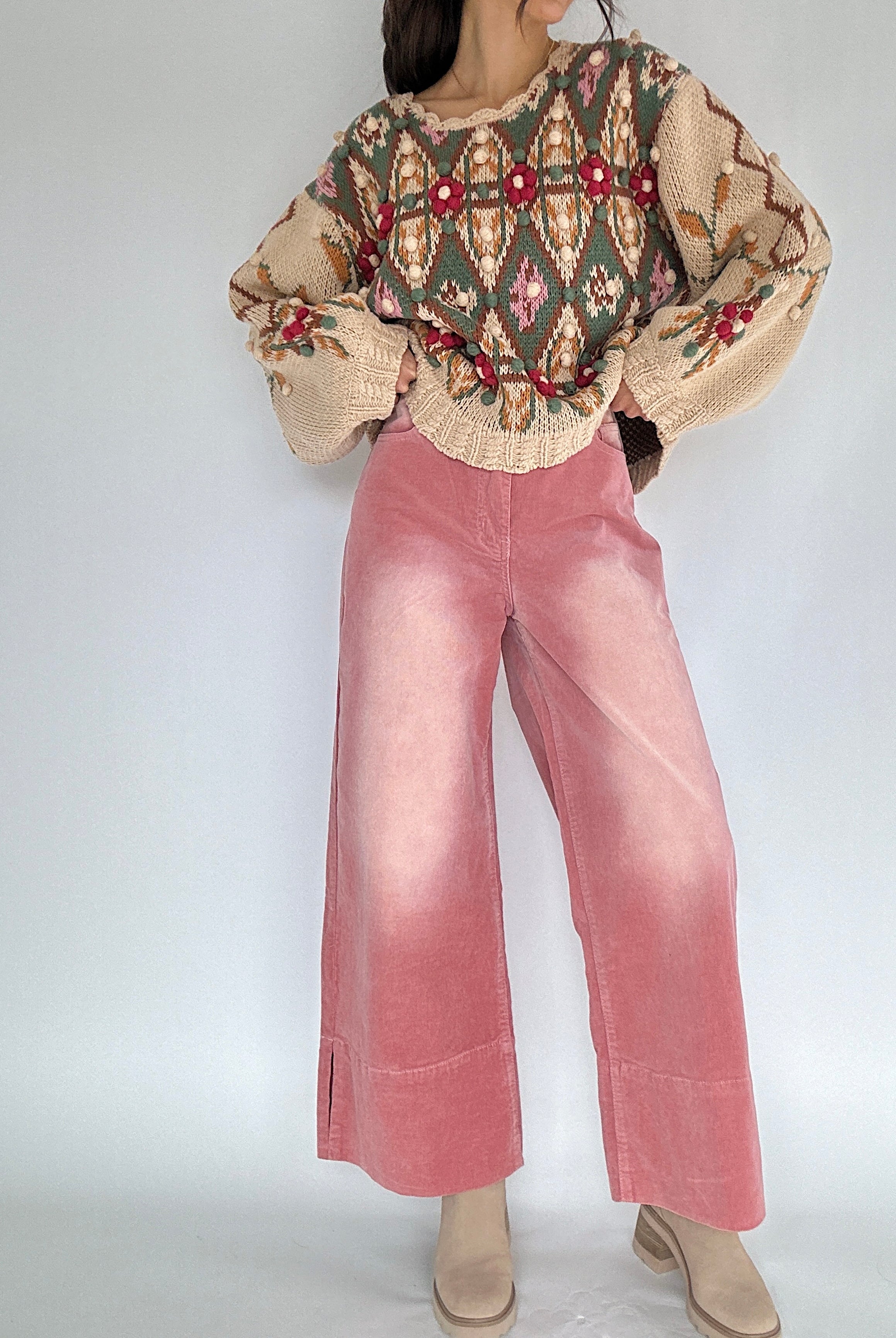 Person wearing a patterned knit sweater and pink corduroy wide leg pants on a white background