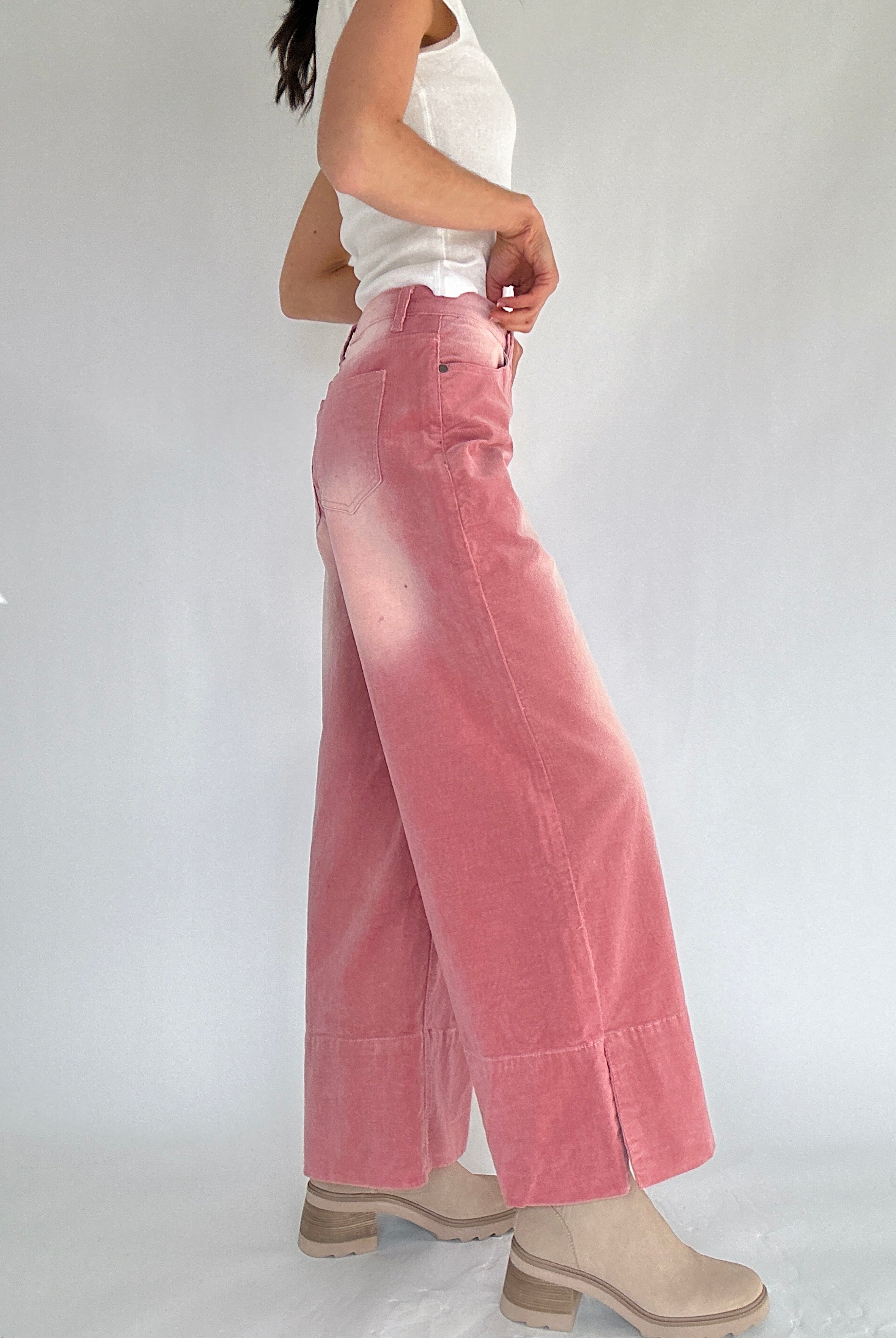 Person wearing pink corduroy wide-leg pants and a white top on a plain background from side