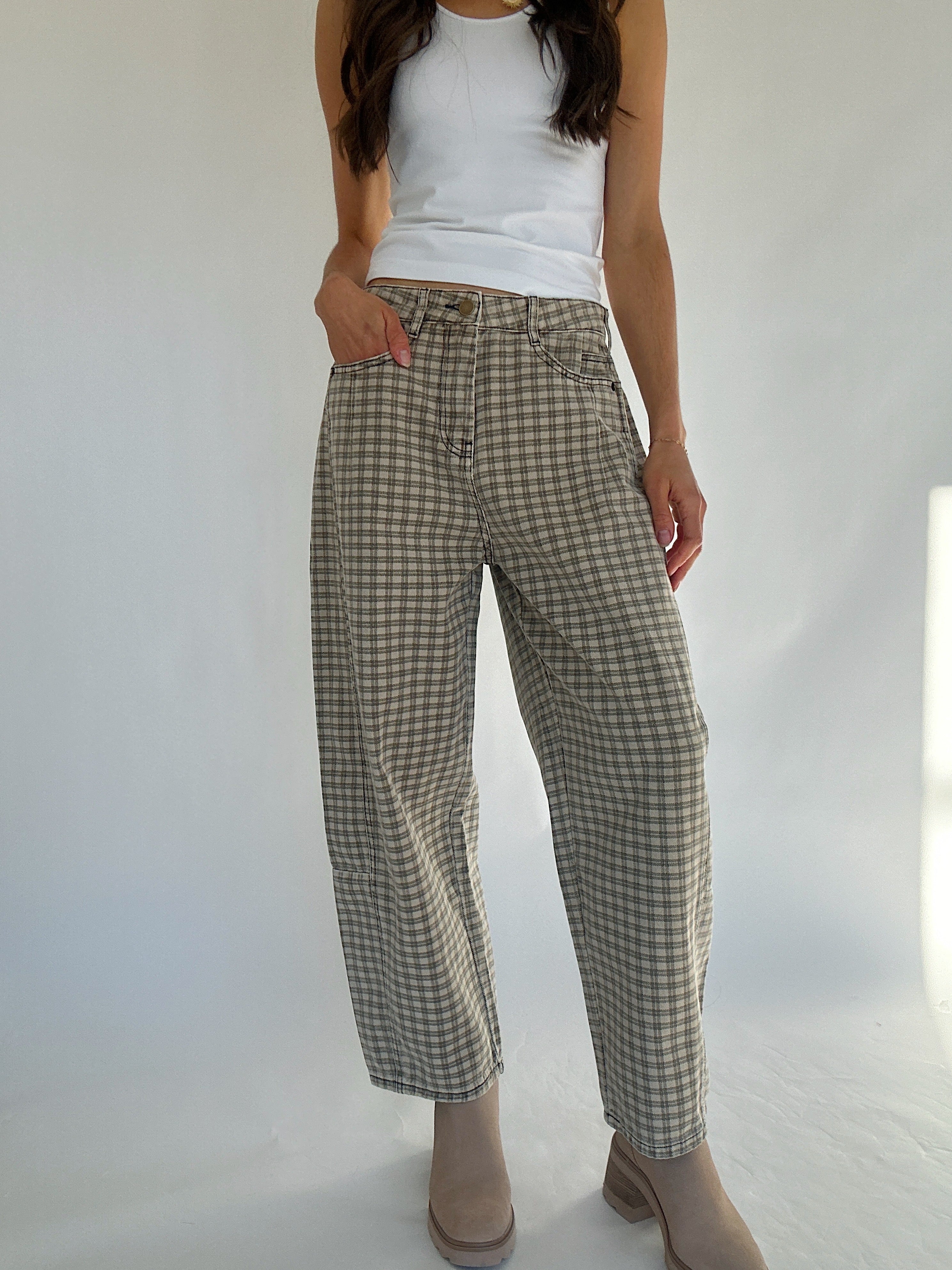 Person wearing plaid barrel pants and a white top on a plain background