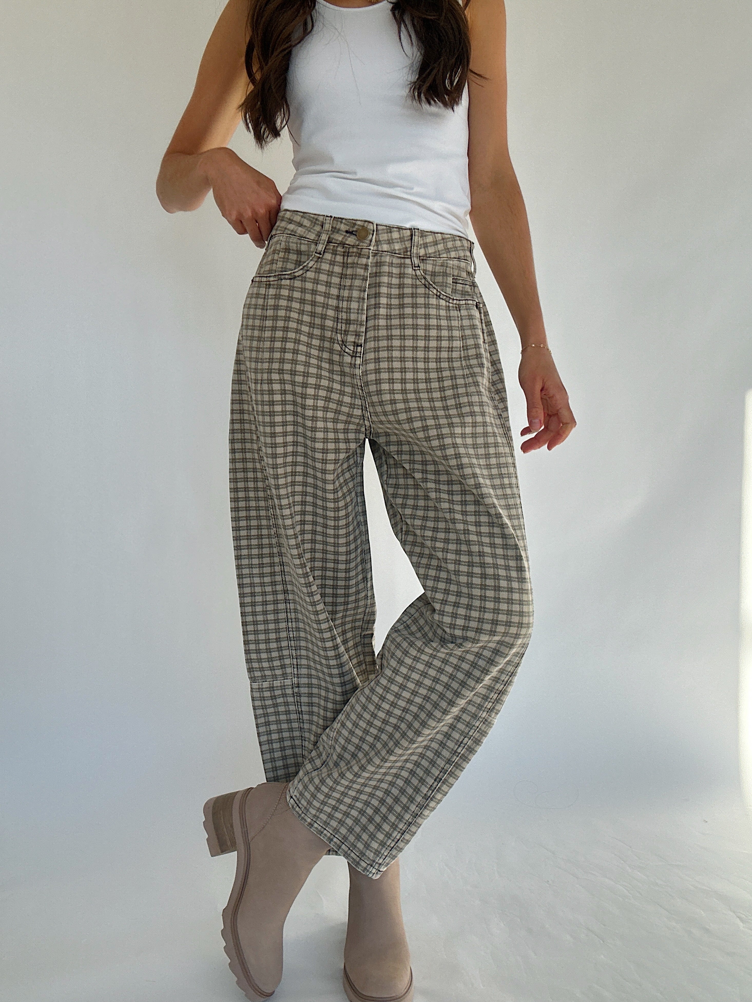 Person wearing plaid pants and a white top on a plain background with legs crossed