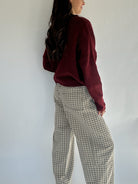 Person wearing a burgundy sweater and checkered pants against a white wall showing side view