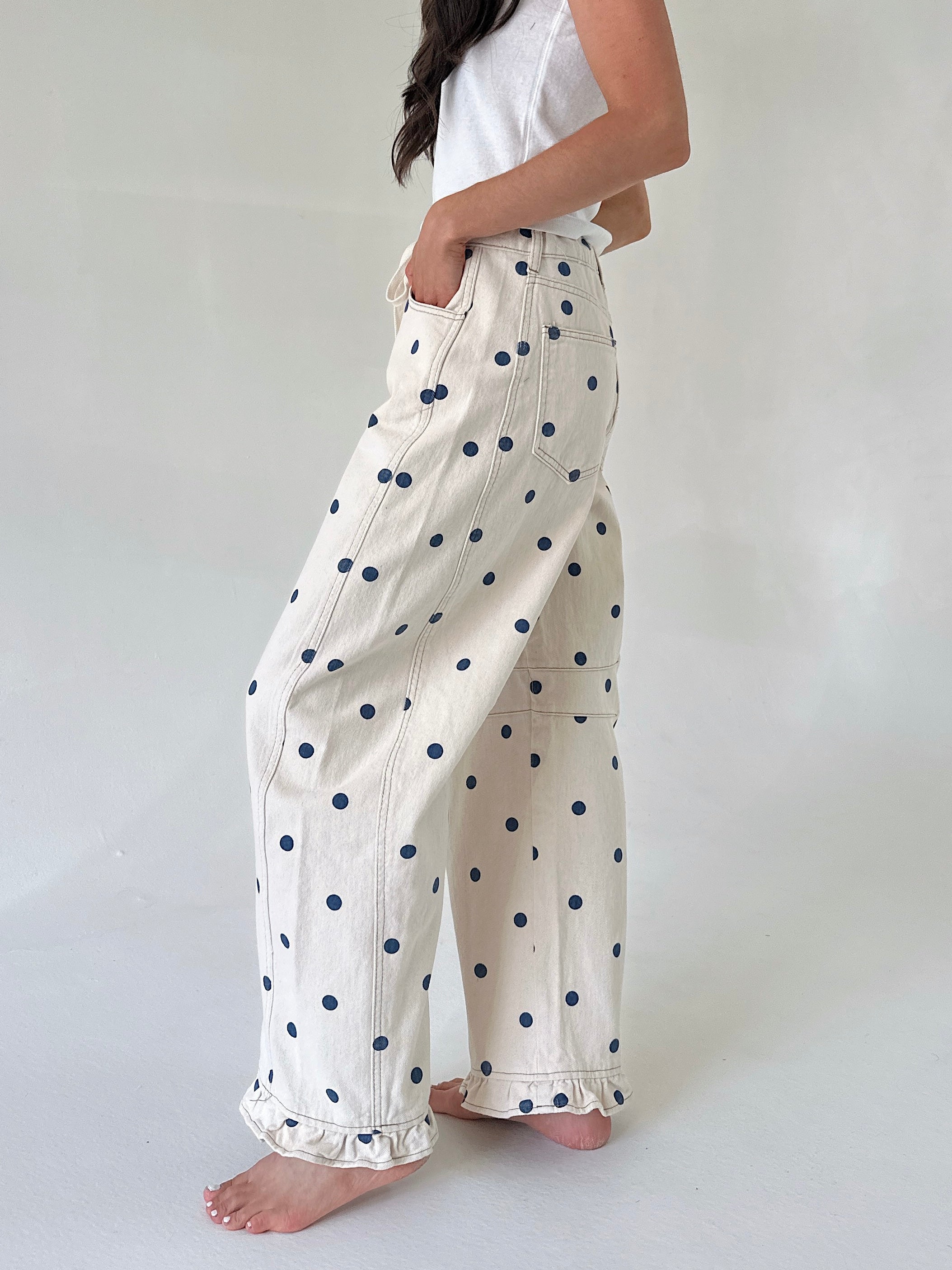 Person wearing white pants with blue polka dots on a plain background from side