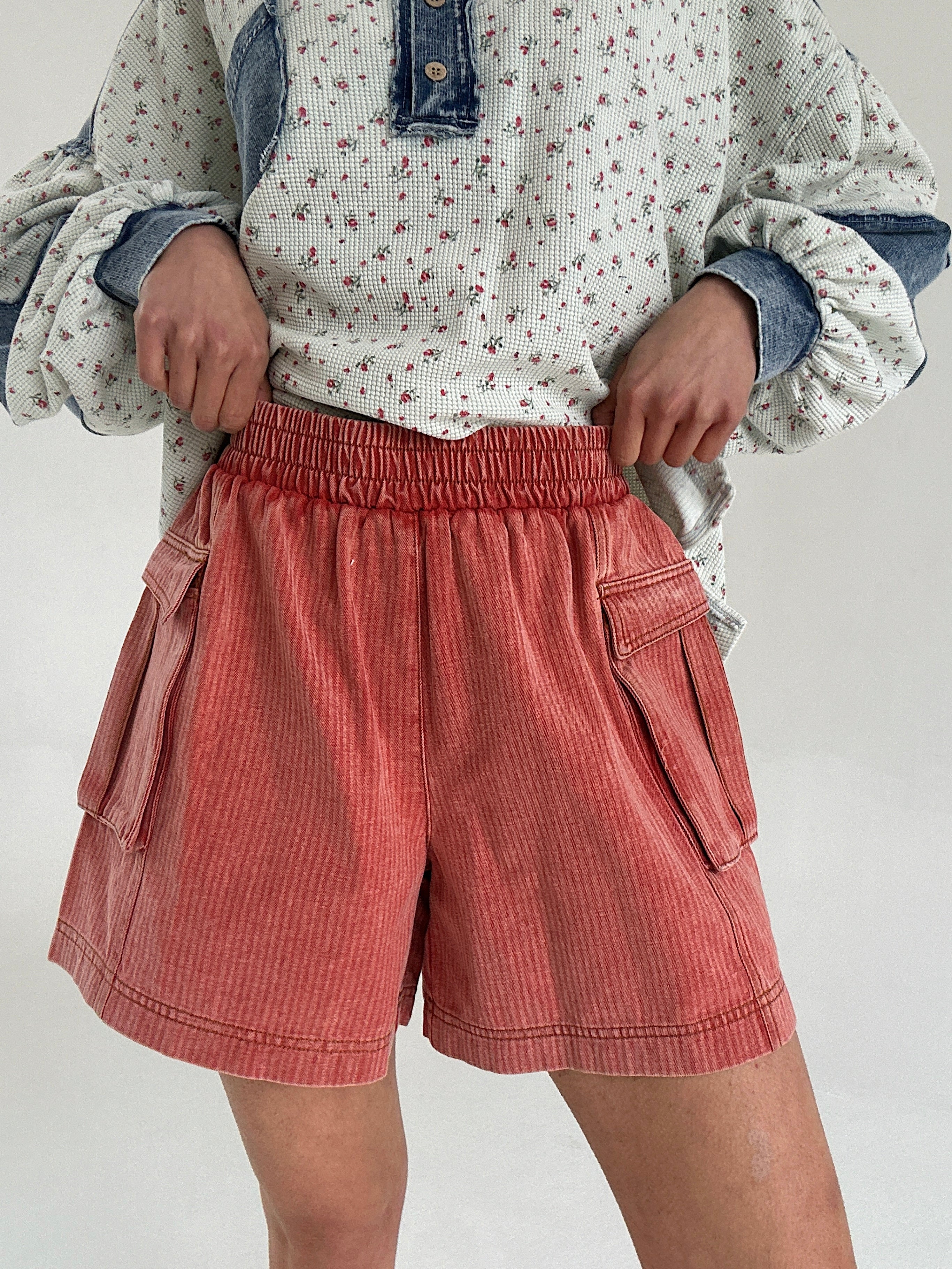 Person wearing a floral shirt and red cargo shorts on a plain background