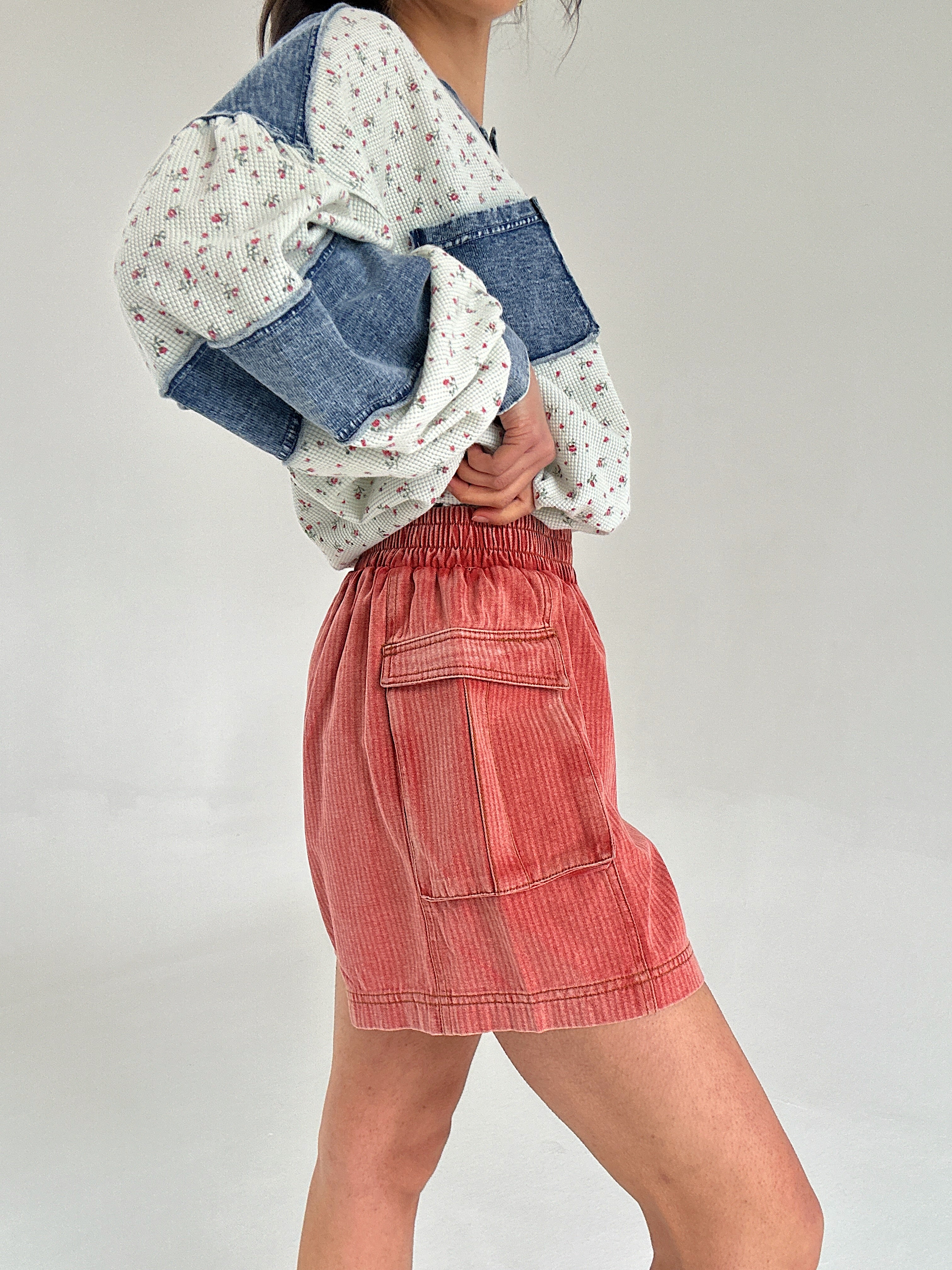 Person wearing a floral top and red cargo shorts on a plain background