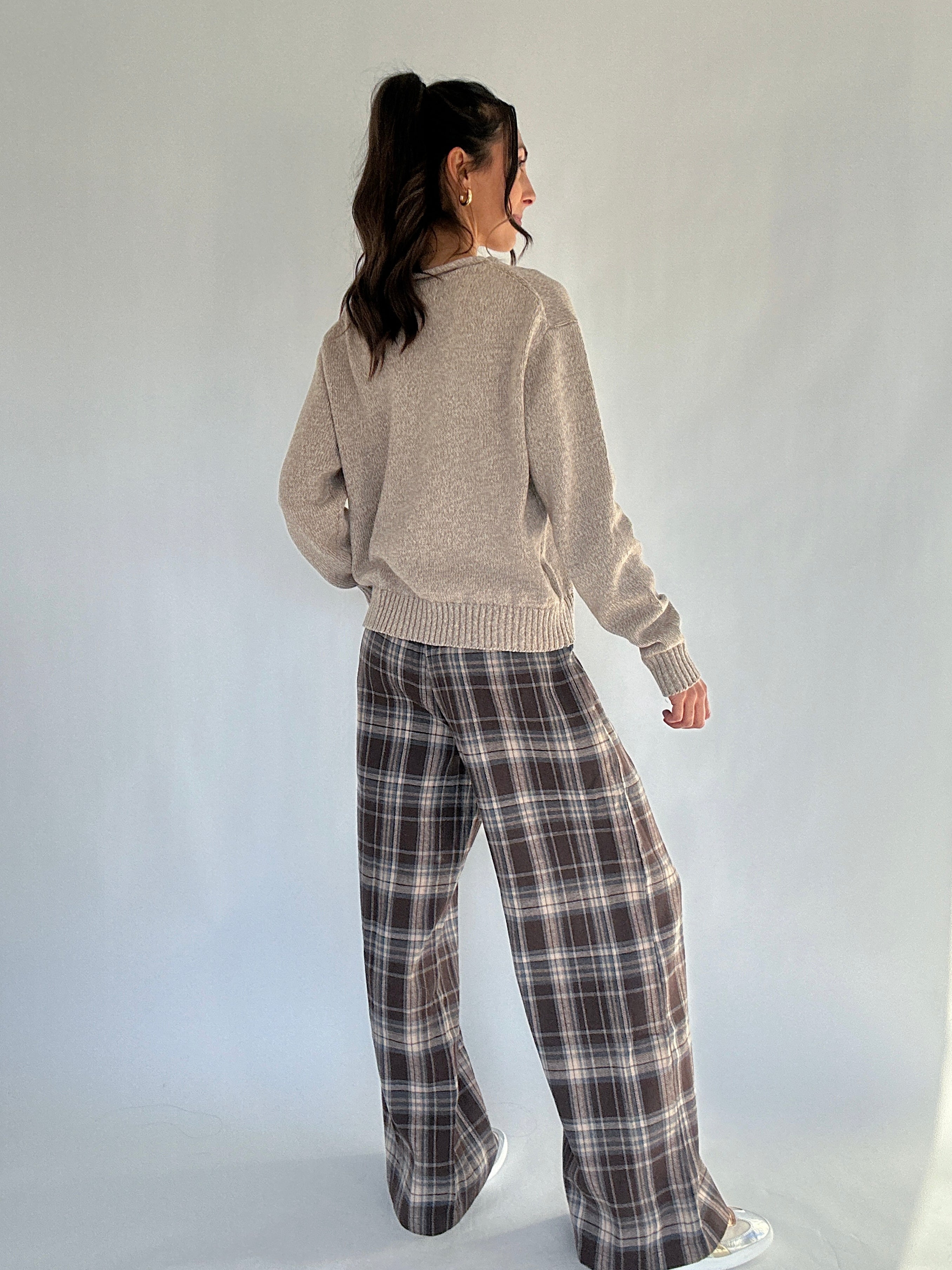Person wearing a beige sweater and plaid pants against a plain background from back