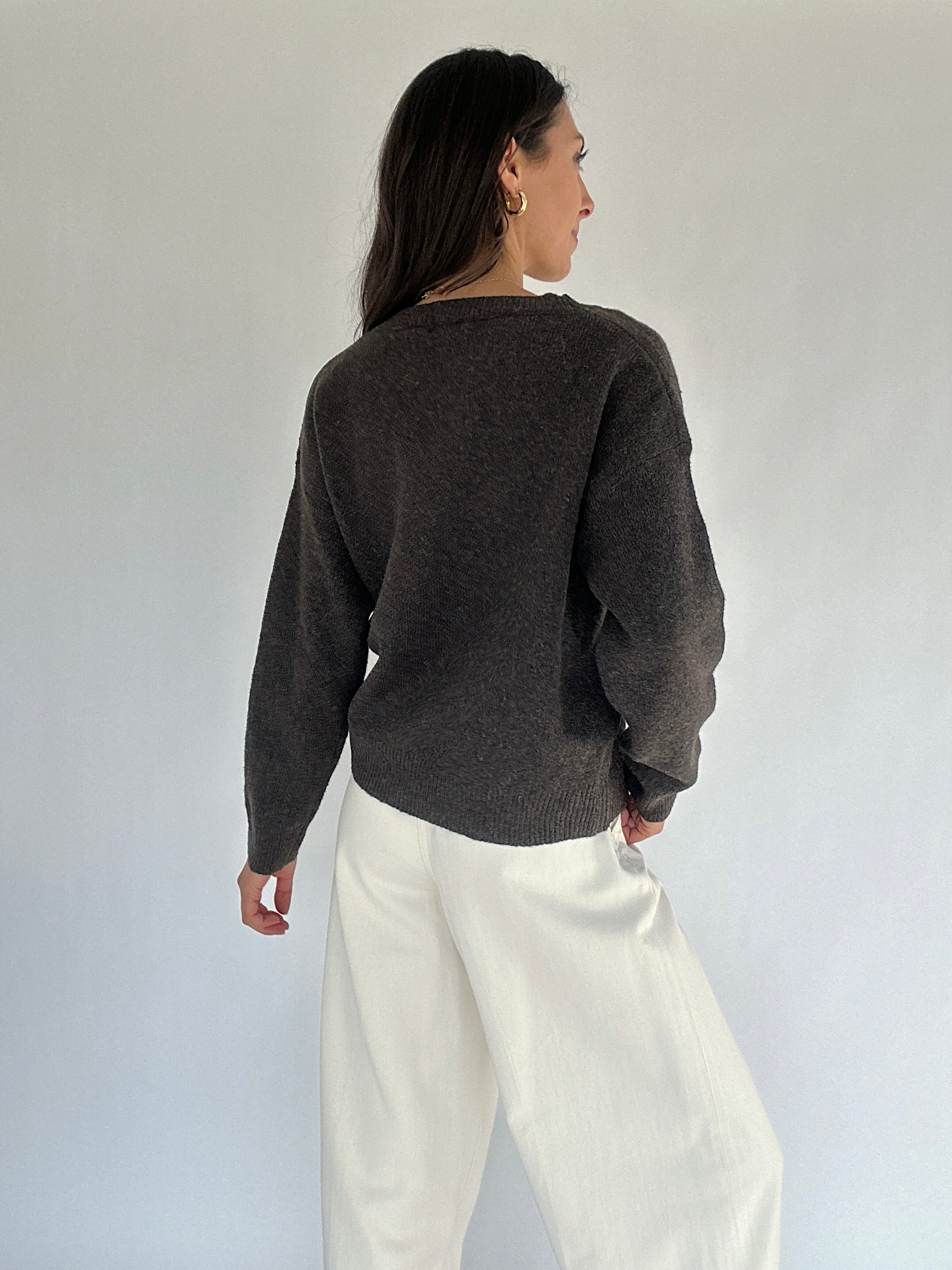 Person wearing a dark brown sweater and white pants against a plain background