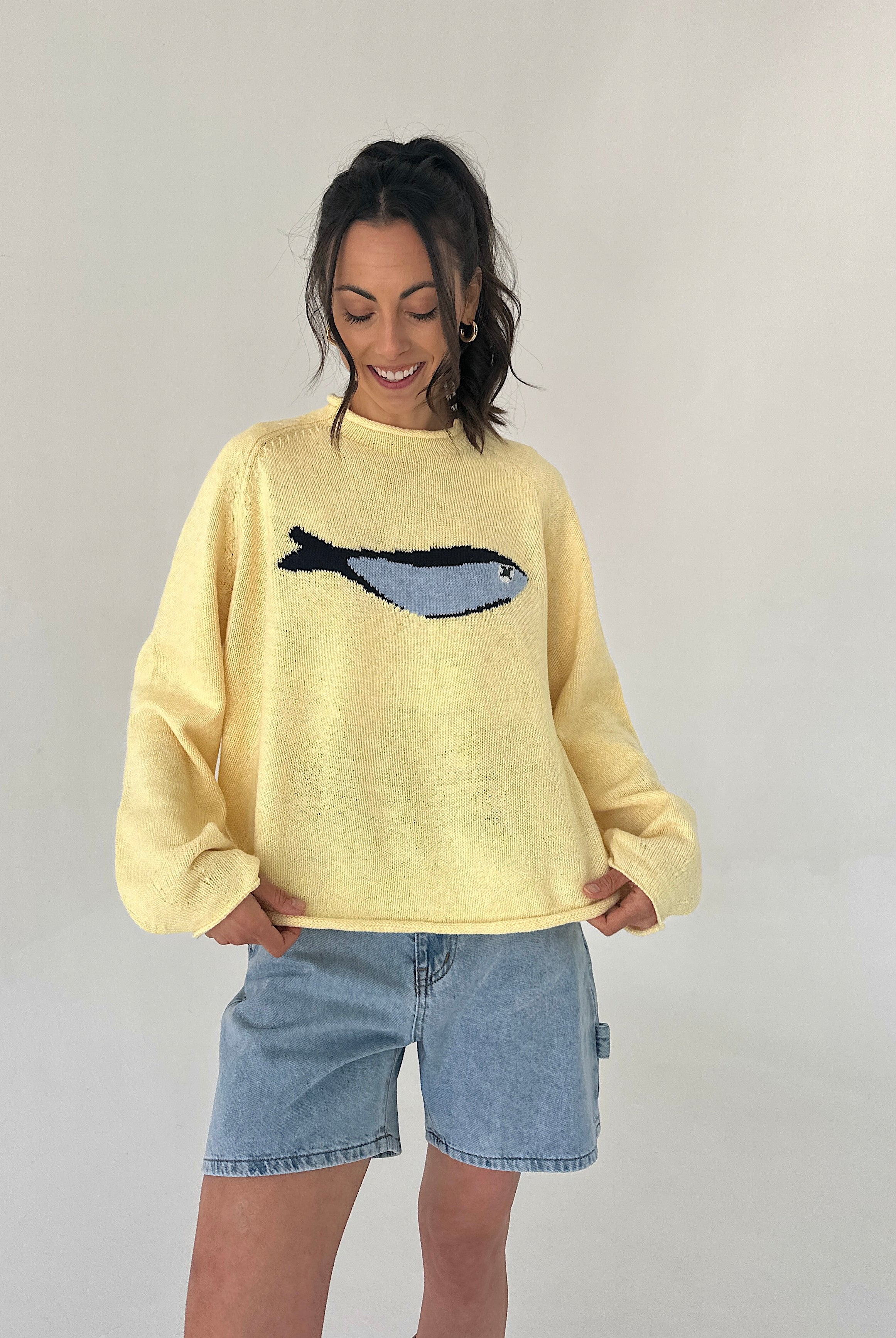Person wearing a yellow sweater with a fish design on a plain background
