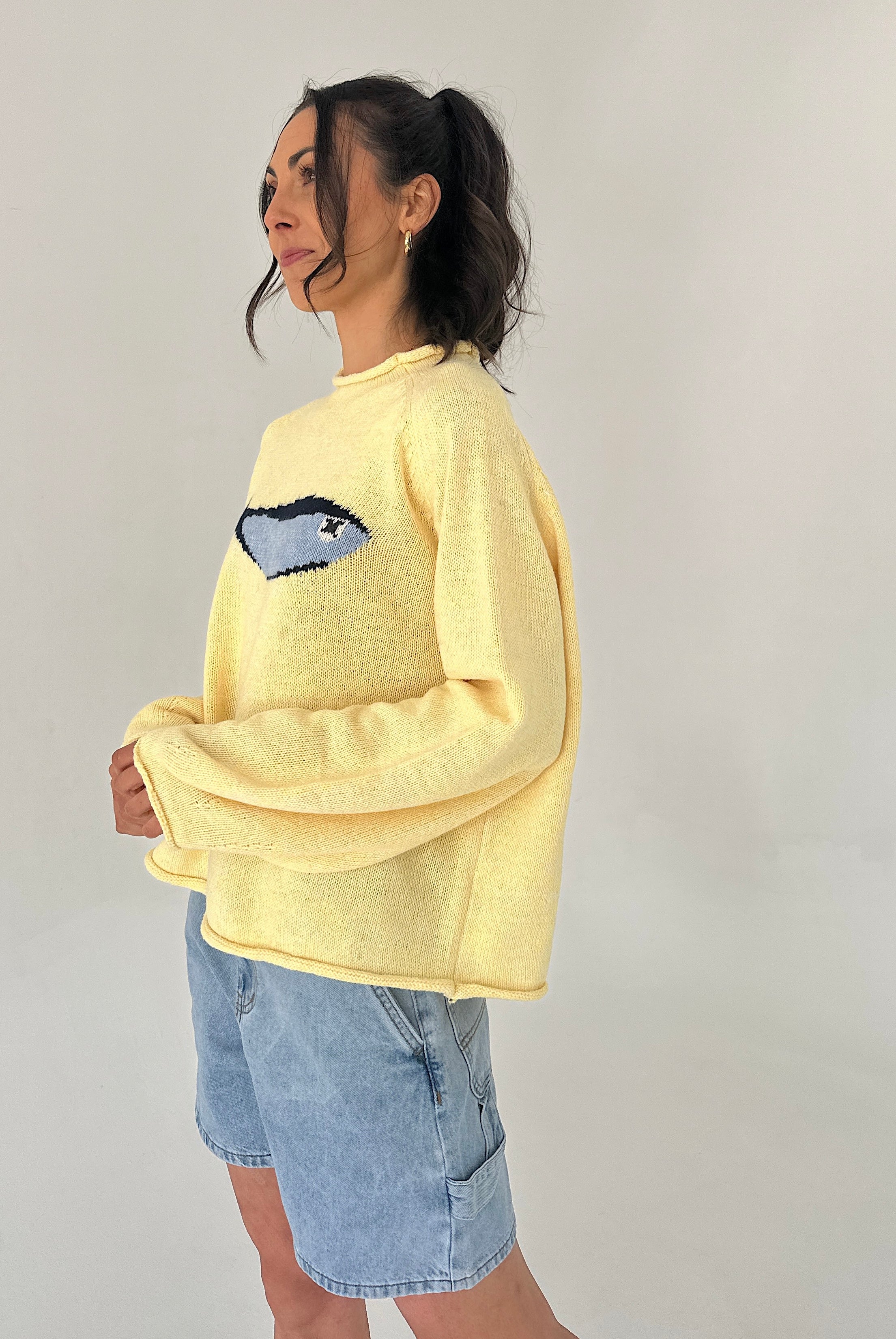 Person wearing a yellow sweater with a blue fish graphic on a plain background