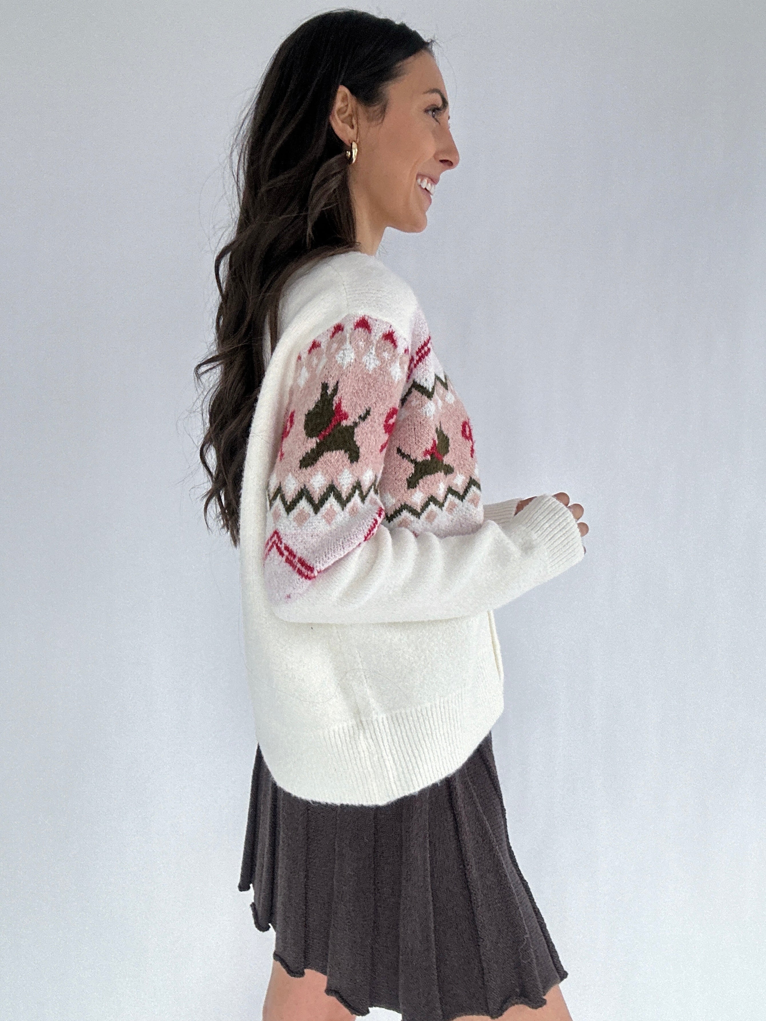 Woman wearing a white cardigan with a patterned design on a plain background showing side