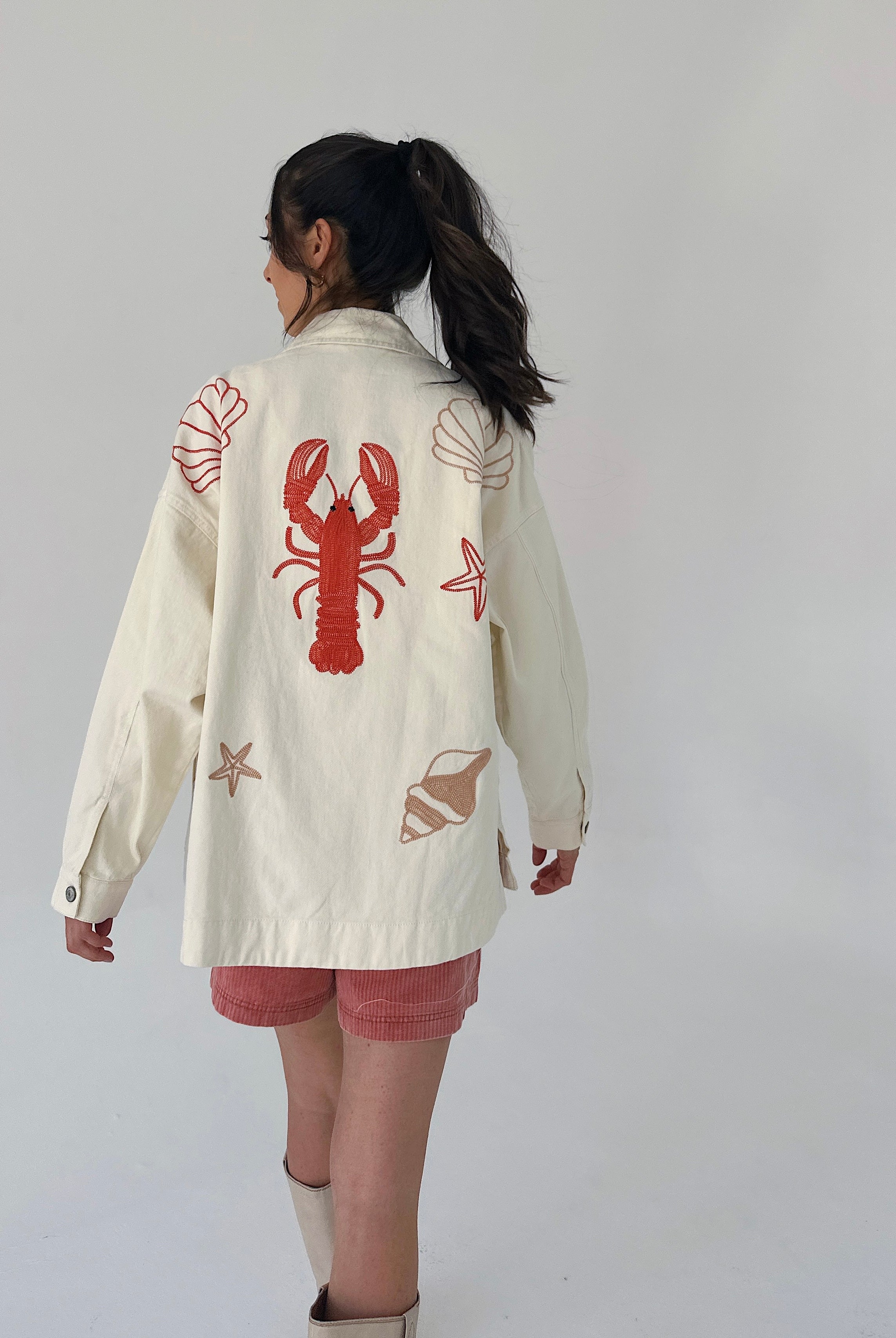 Person wearing a cream-colored jacket with red lobster design on a plain background