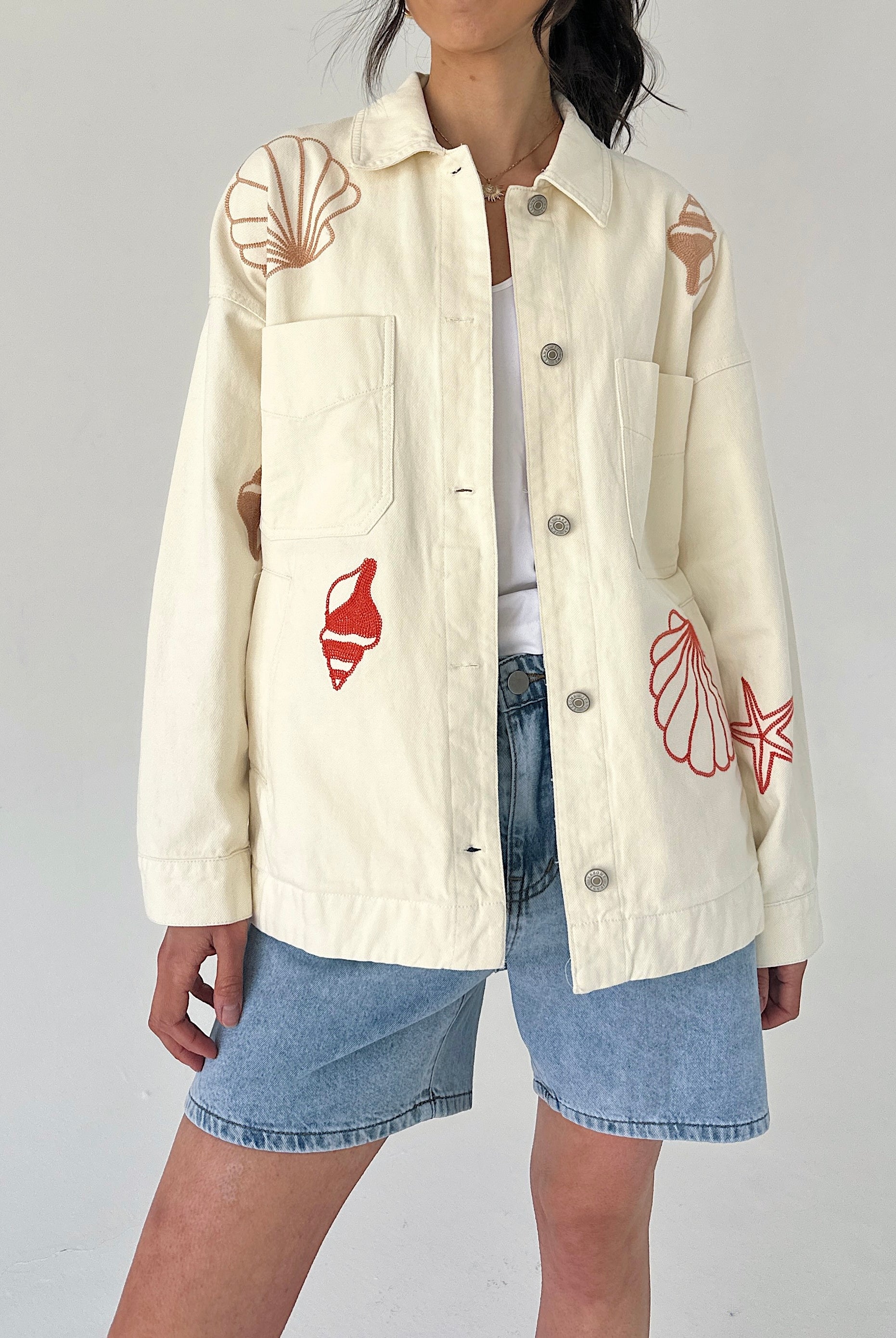 Person wearing a cream jacket with red shell designs on a plain background