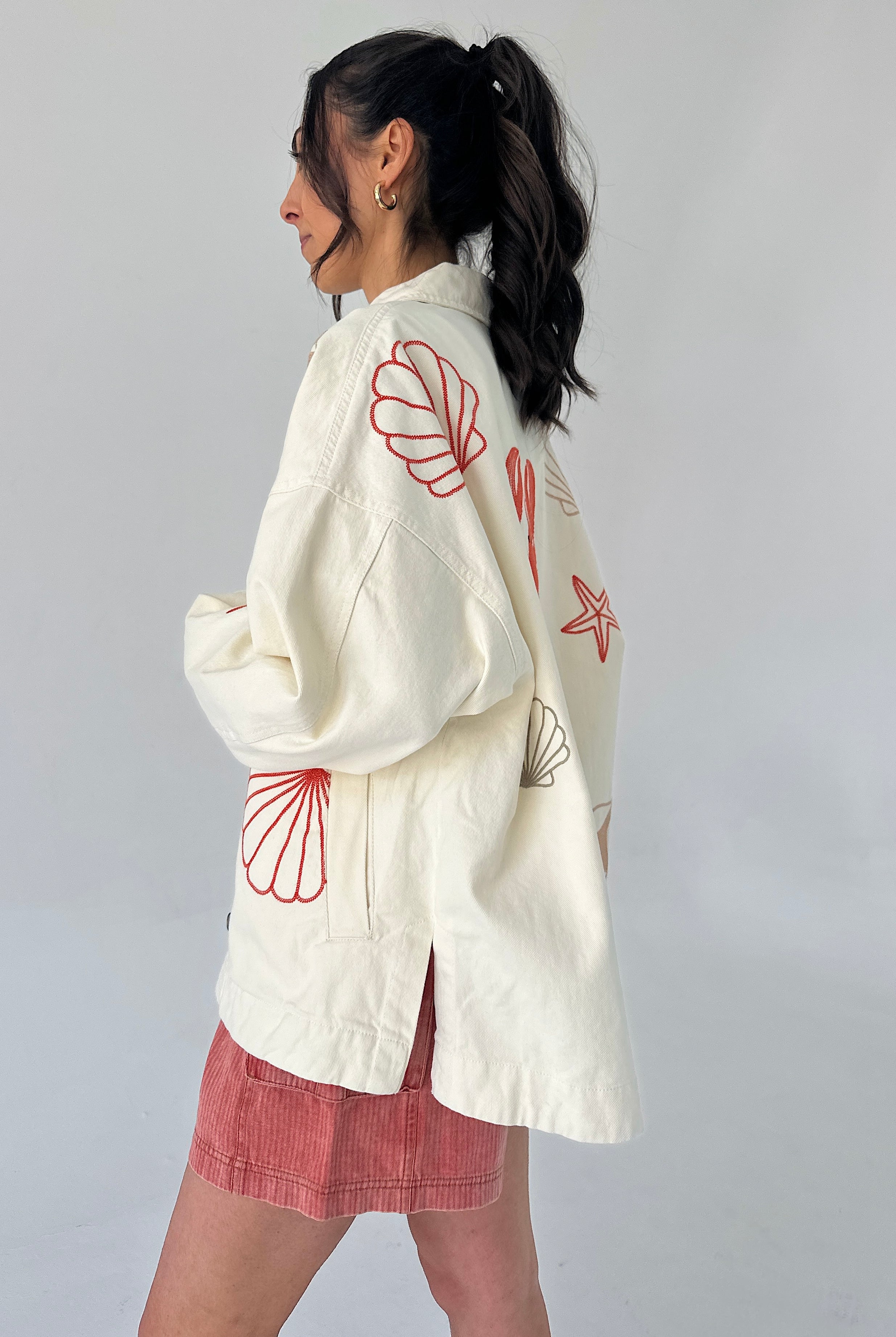 Person wearing a white jacket with red seashell patterns on the back, standing against a plain background