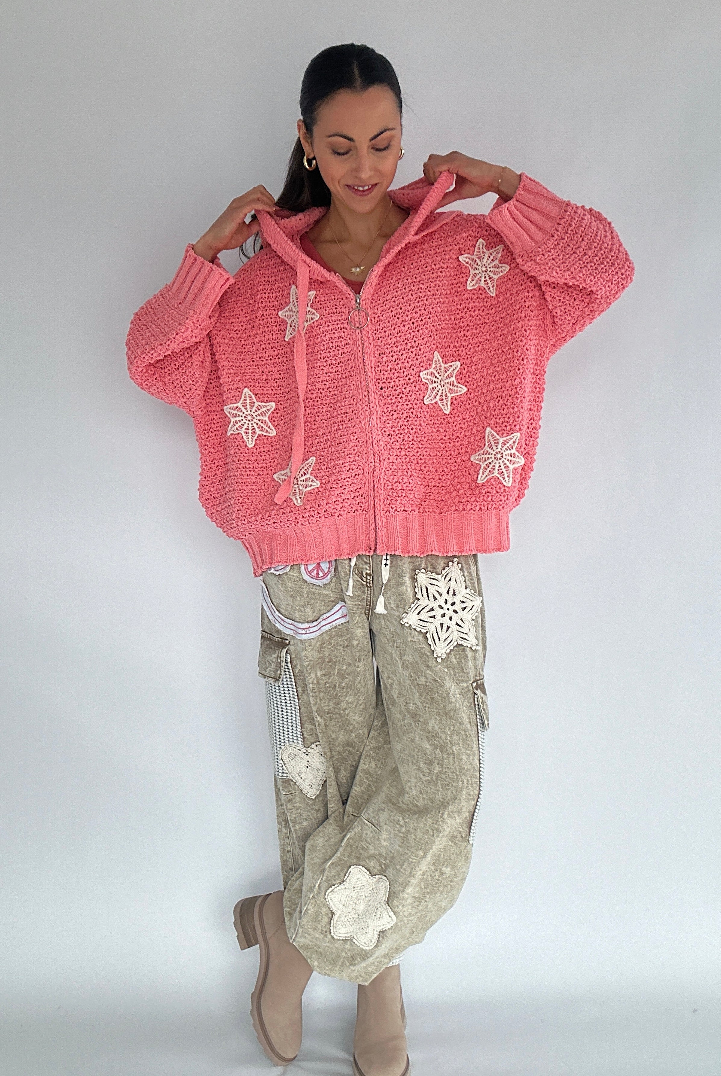 Woman wearing a pink knitted zip up hoodie with snowflake patterns on a plain background