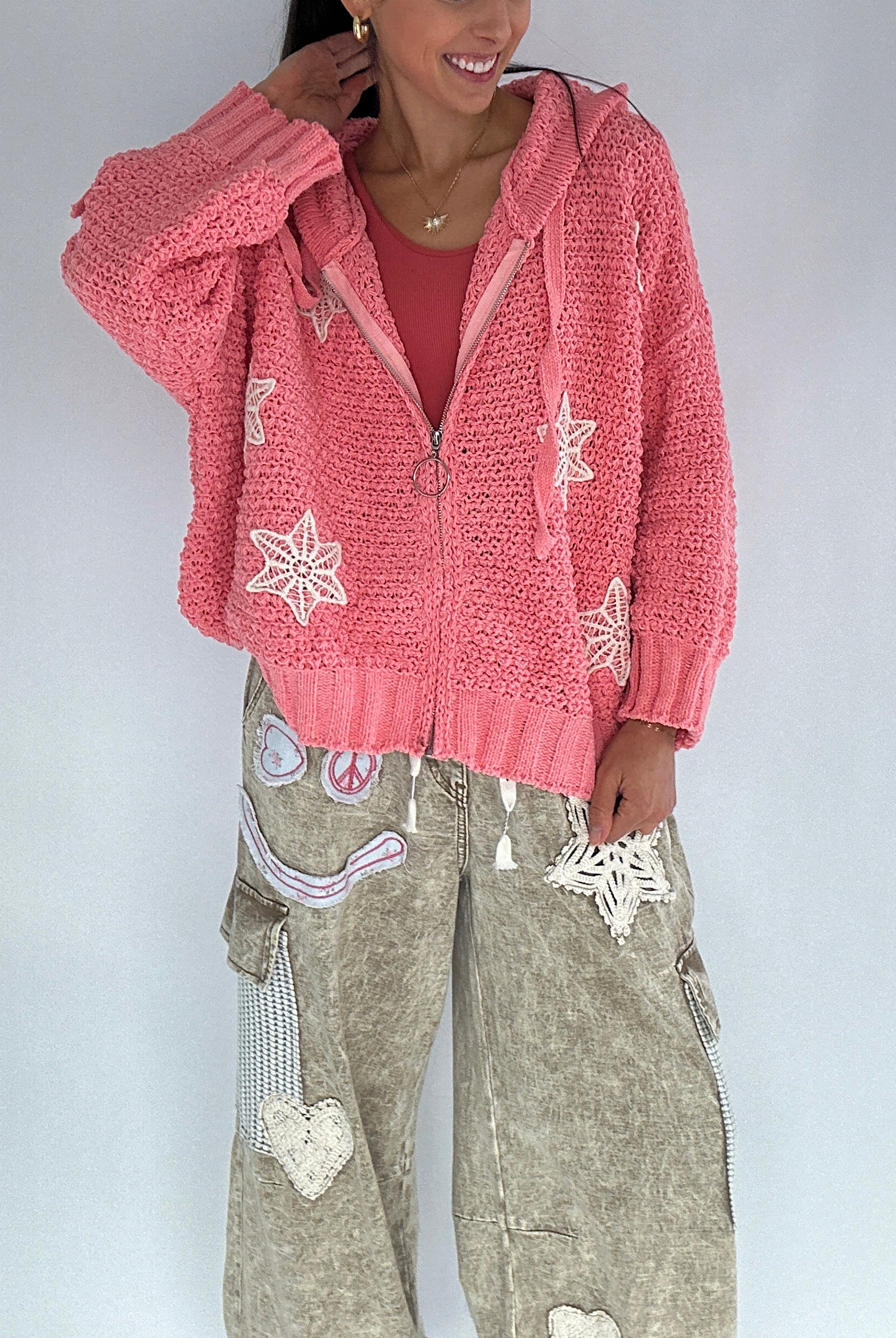 Person wearing a pink zip up chenille hooded cardigan with crochet snowflake patterns on a plain background