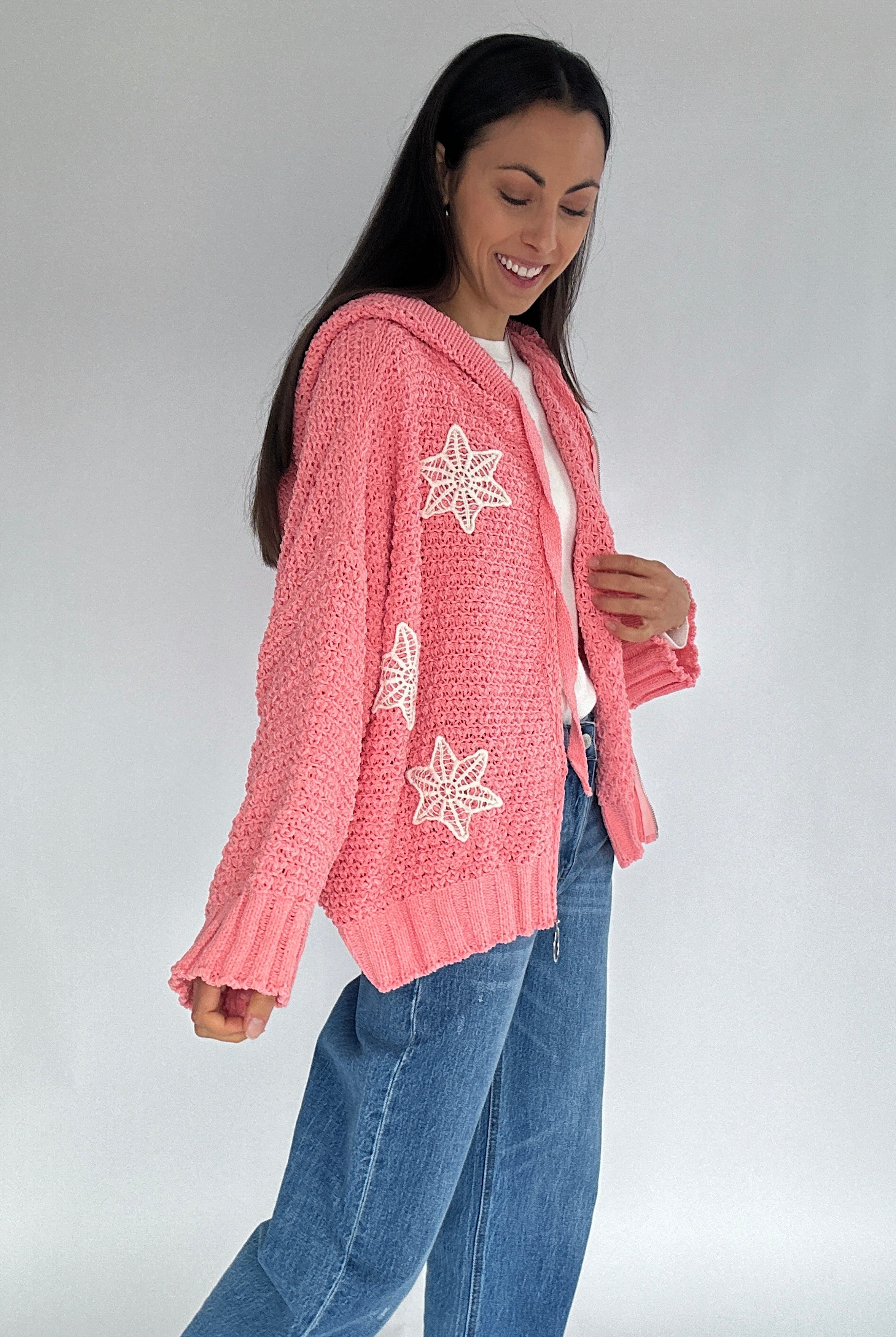 Woman wearing a pink cardigan with crochet patterns on a plain background from side